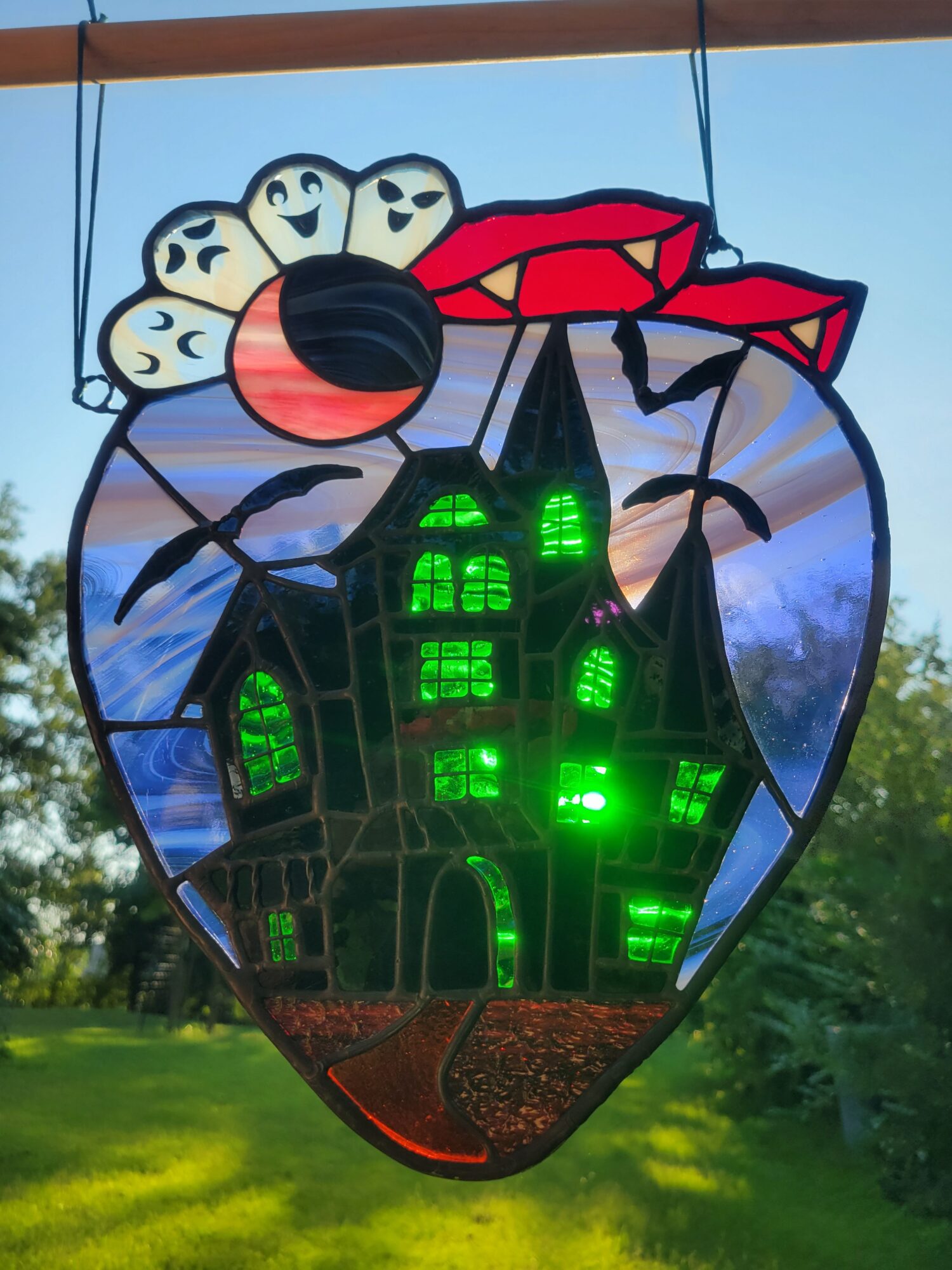 Colorful ladybug-shaped lantern with green lights, set outdoors with trees and grass in the background.
