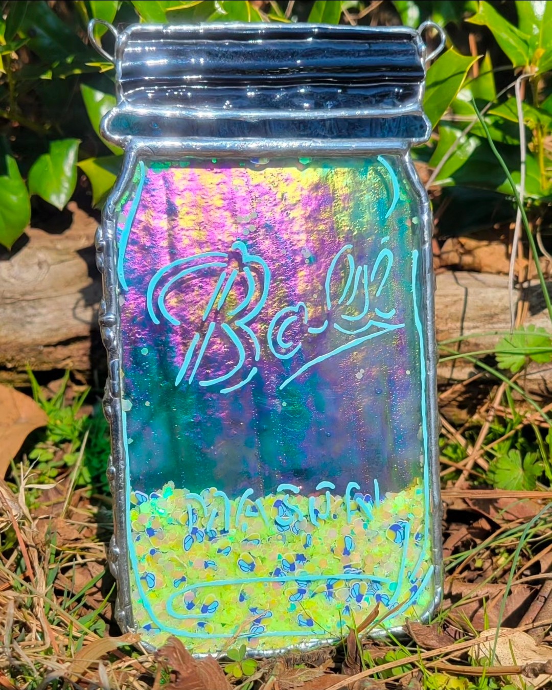 A shiny, holographic jar-shaped object with the word 'Bae' written on it, placed outdoors among green plants and soil.