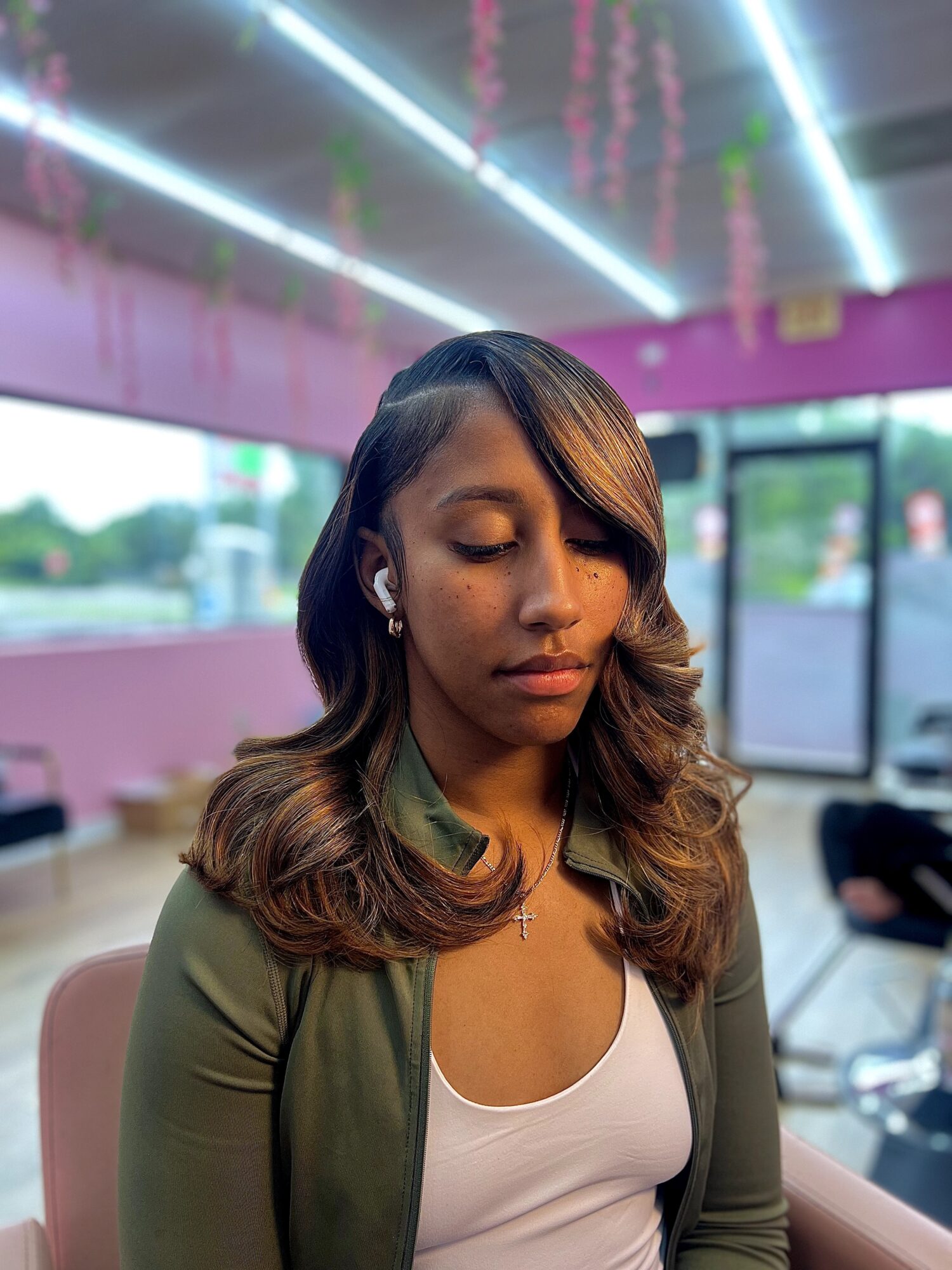 Young woman with wavy hair and earrings, eyes closed, indoors with pink walls and ceiling lights.