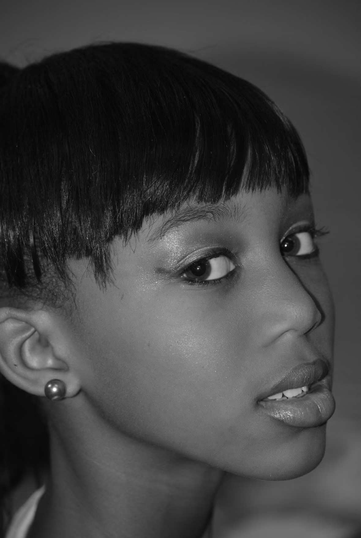 Close-up of a woman with short hair, earrings, and makeup, looking sideways, in black and white.