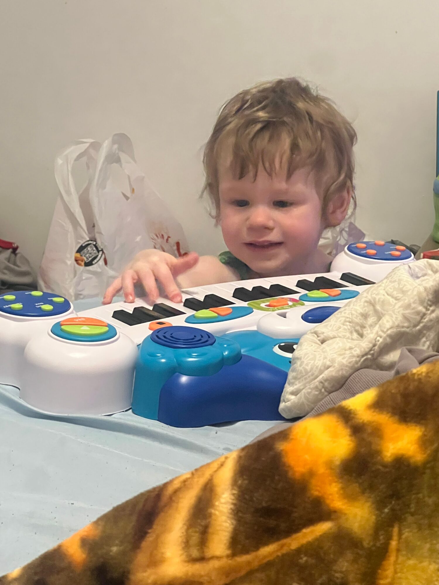 Child playing with a colorful electronic toy on a table, with a blanket nearby, against a plain background.
