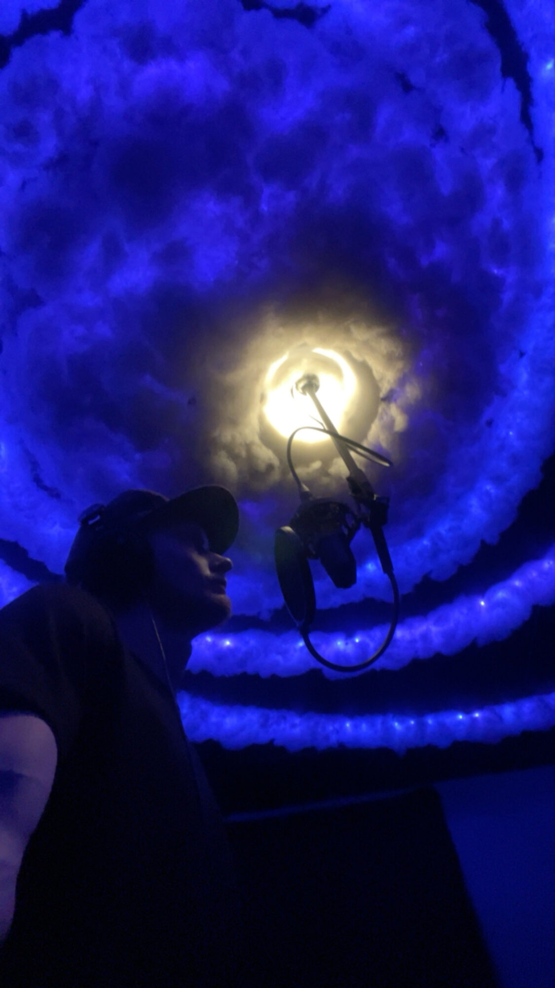 Person standing in front of a circular, illuminated ceiling with blue and yellow lighting effects.