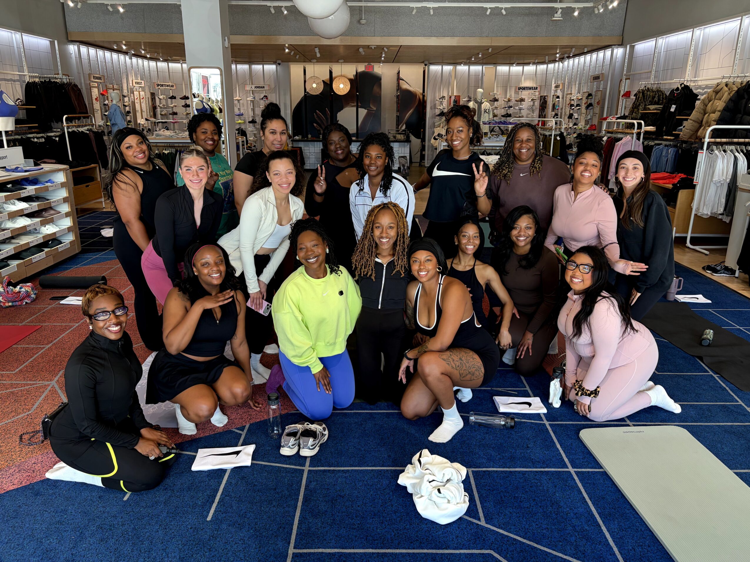 Group of women and girls posing inside a clothing store, some sitting and some standing, smiling at the camera.