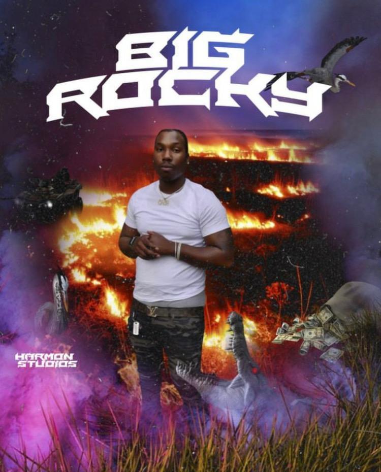 Young man standing outdoors with a fiery background, purple fog, and a flying dinosaur silhouette, with bold text 'Big Rocks'.
