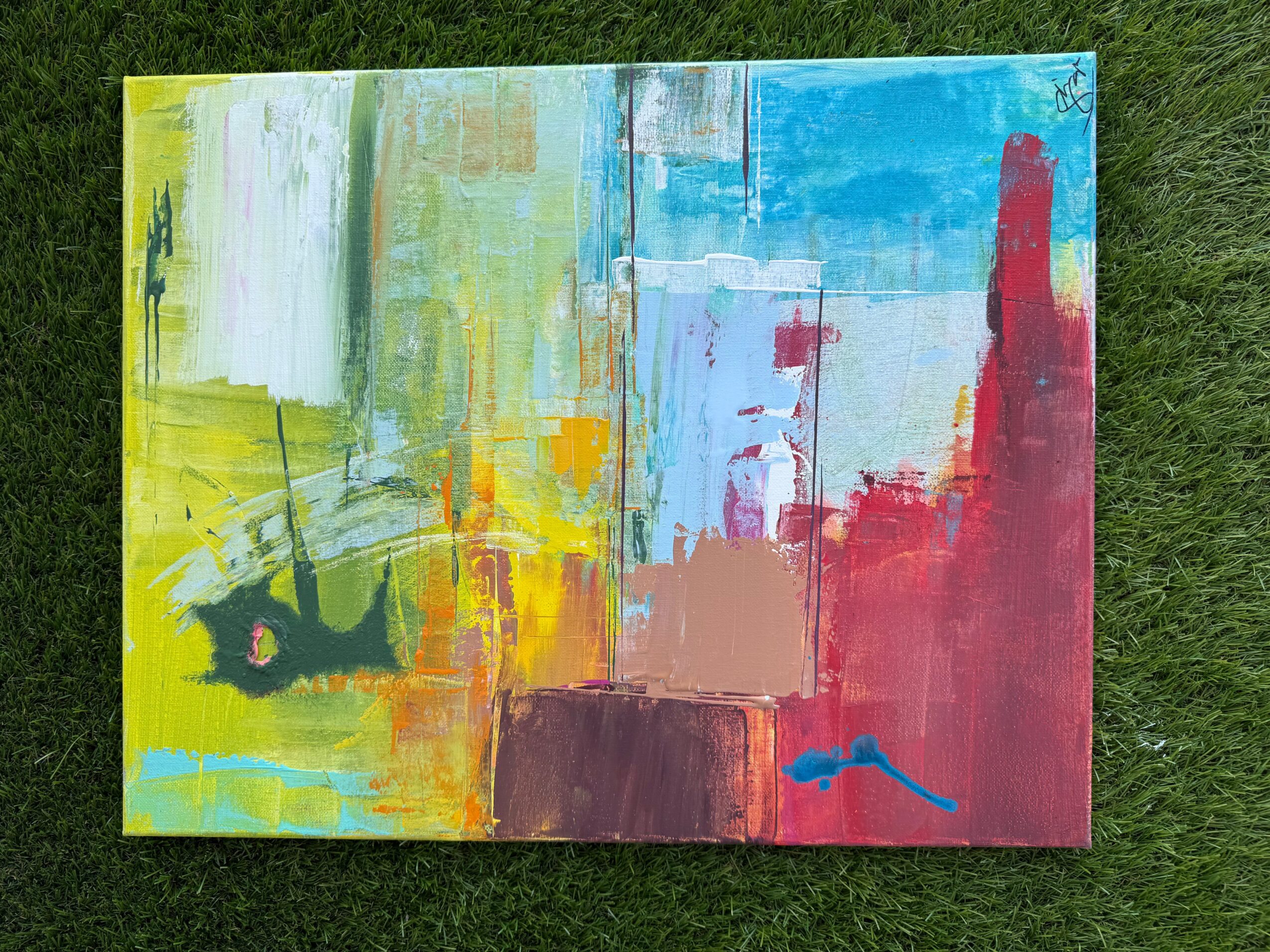 Abstract painting with yellow, green, blue, and red colors on canvas, placed on grass.