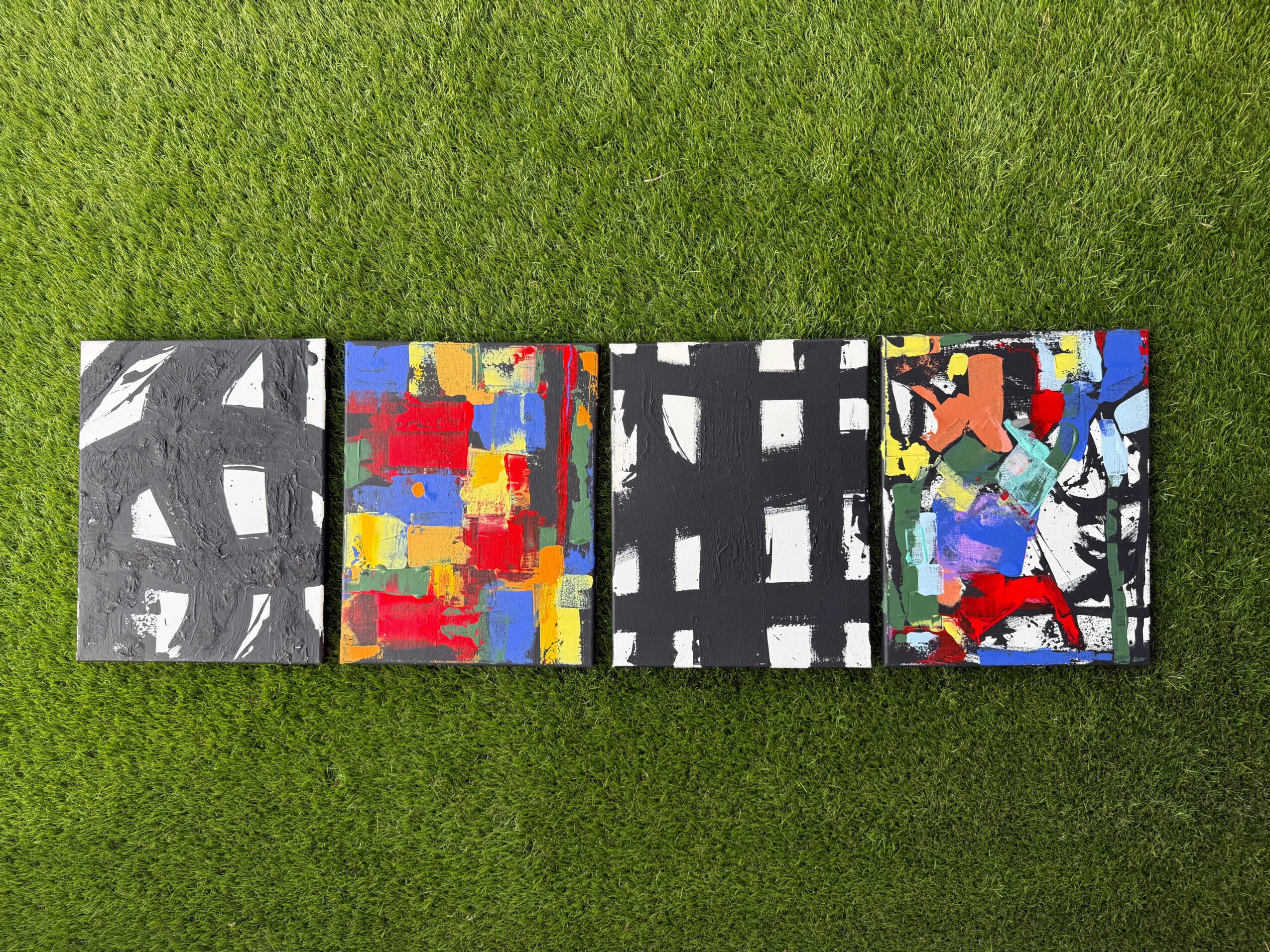 Four colorful abstract paintings laid out on grass, each with different patterns and colors.