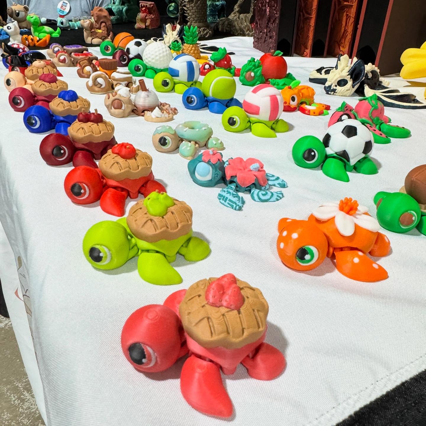 Colorful toy animals and creatures arranged on a white tablecloth, including frogs, pandas, and other animals, outdoors.