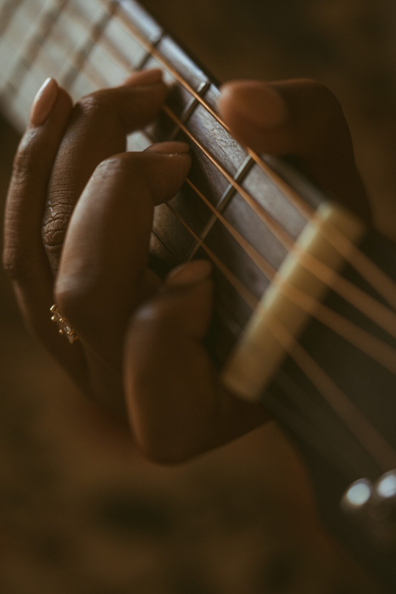Close-up of a person's hand pressing guitar strings on fretboard, with warm lighting and blurred background.