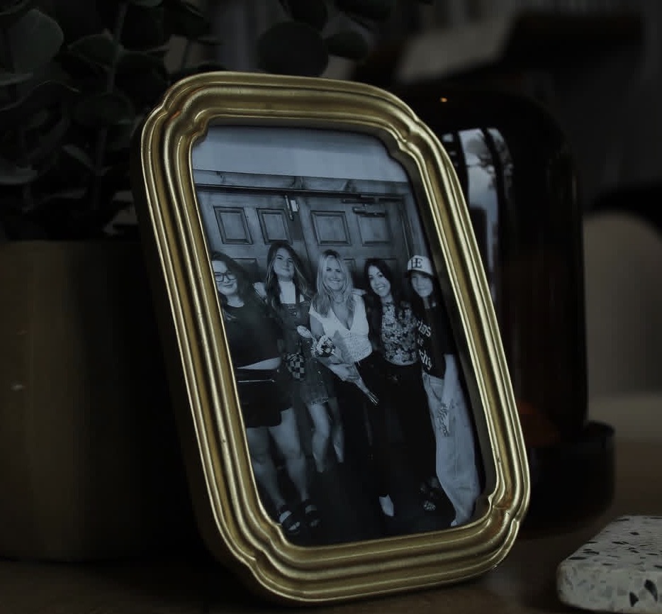 Photograph of four people in a decorative frame, standing indoors with wooden paneling in the background.