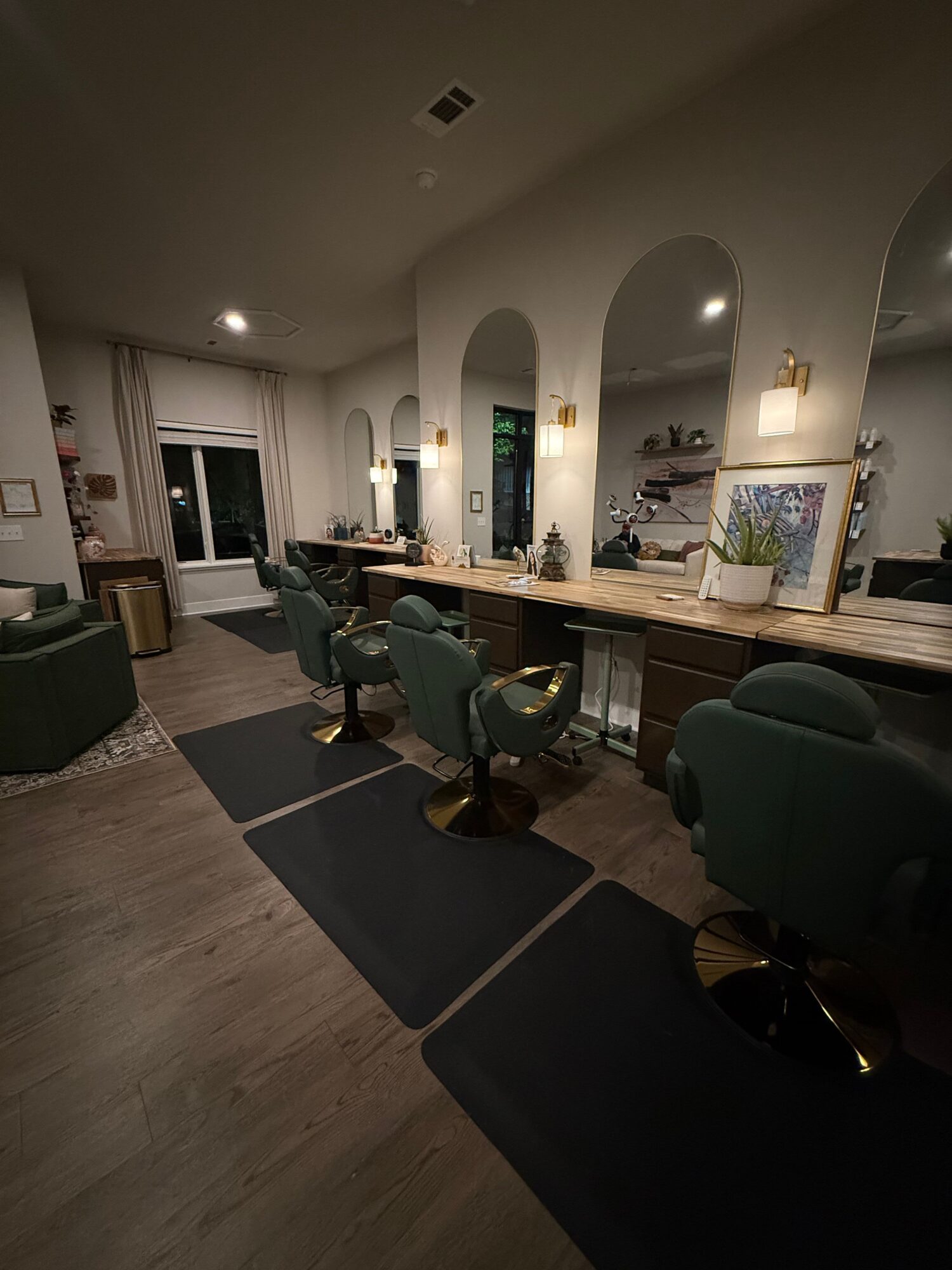 Living room with a dining table, chairs, and a green armchair, illuminated by ceiling lights, with a window and artwork on the wall.