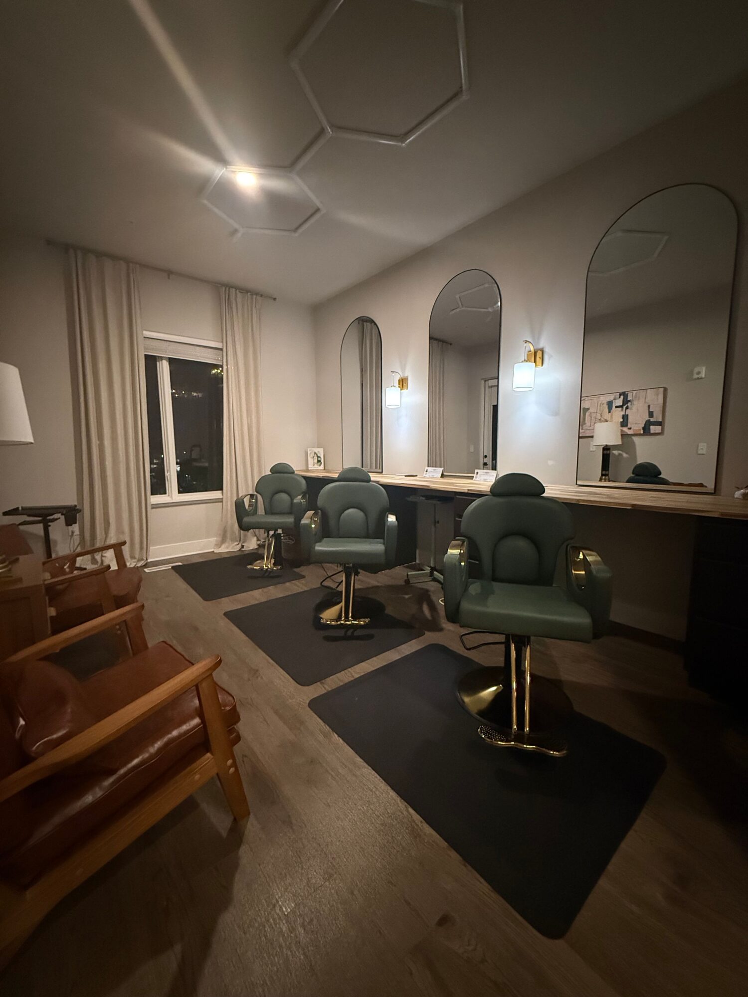 Living room with green chairs, a mirror, and a window, viewed from the doorway, with wooden flooring and a small wooden table.