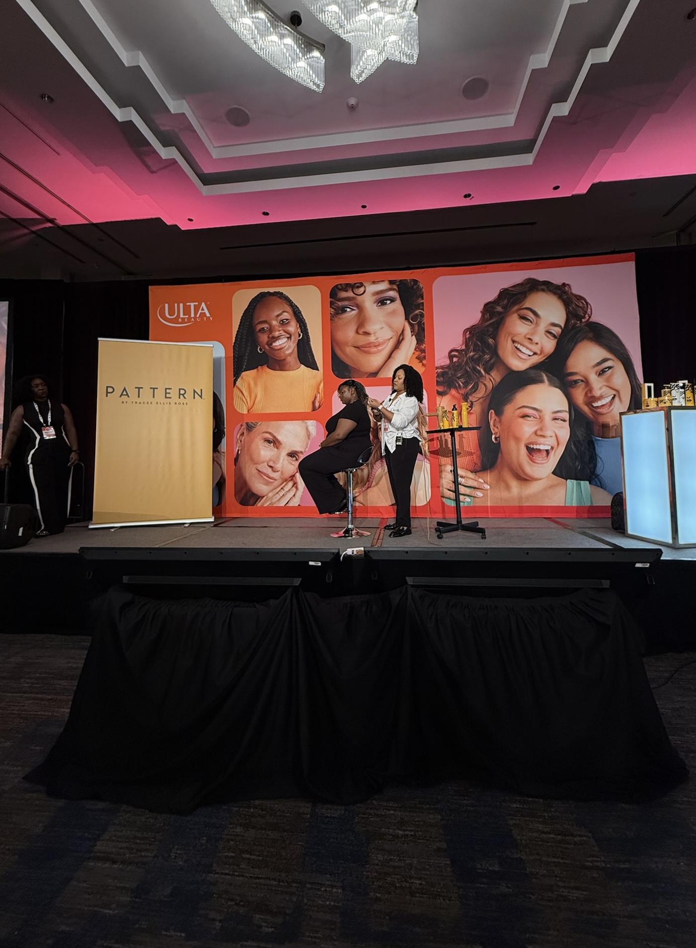 Stage with large backdrop of diverse smiling faces, a woman speaking at a podium, and a banner reading 'PATTERN'.