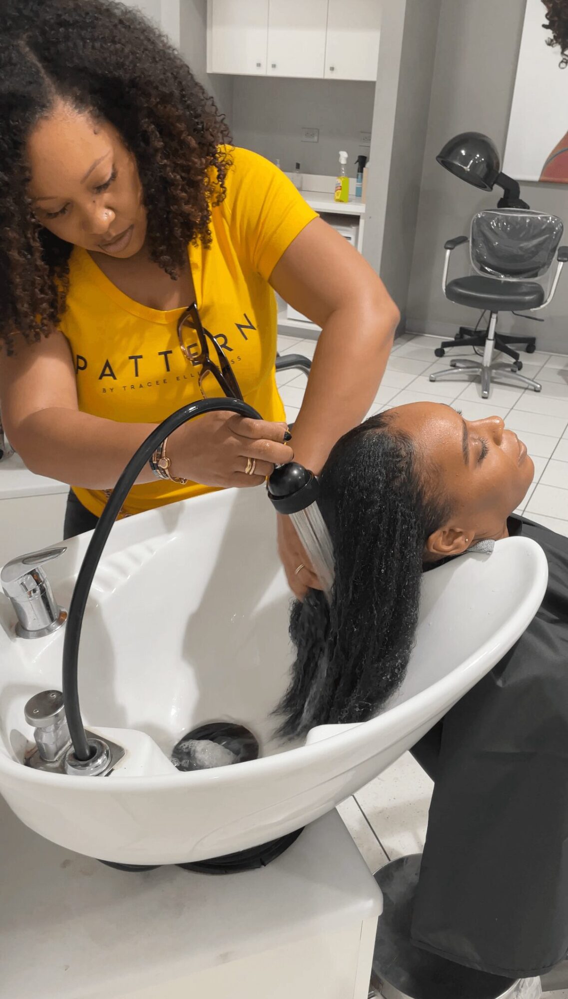 Woman washing a person's hair in a salon sink, with hair flowing into the basin, in a professional setting.