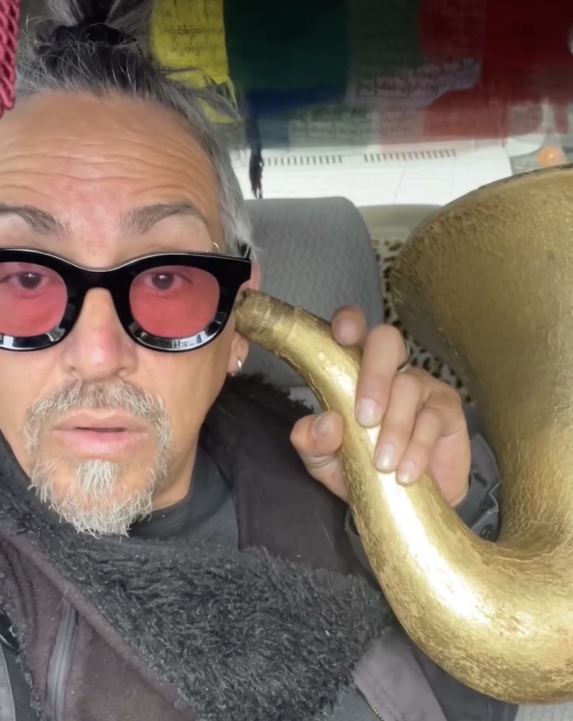 Person with sunglasses holding a large, curved, golden object inside a vehicle.