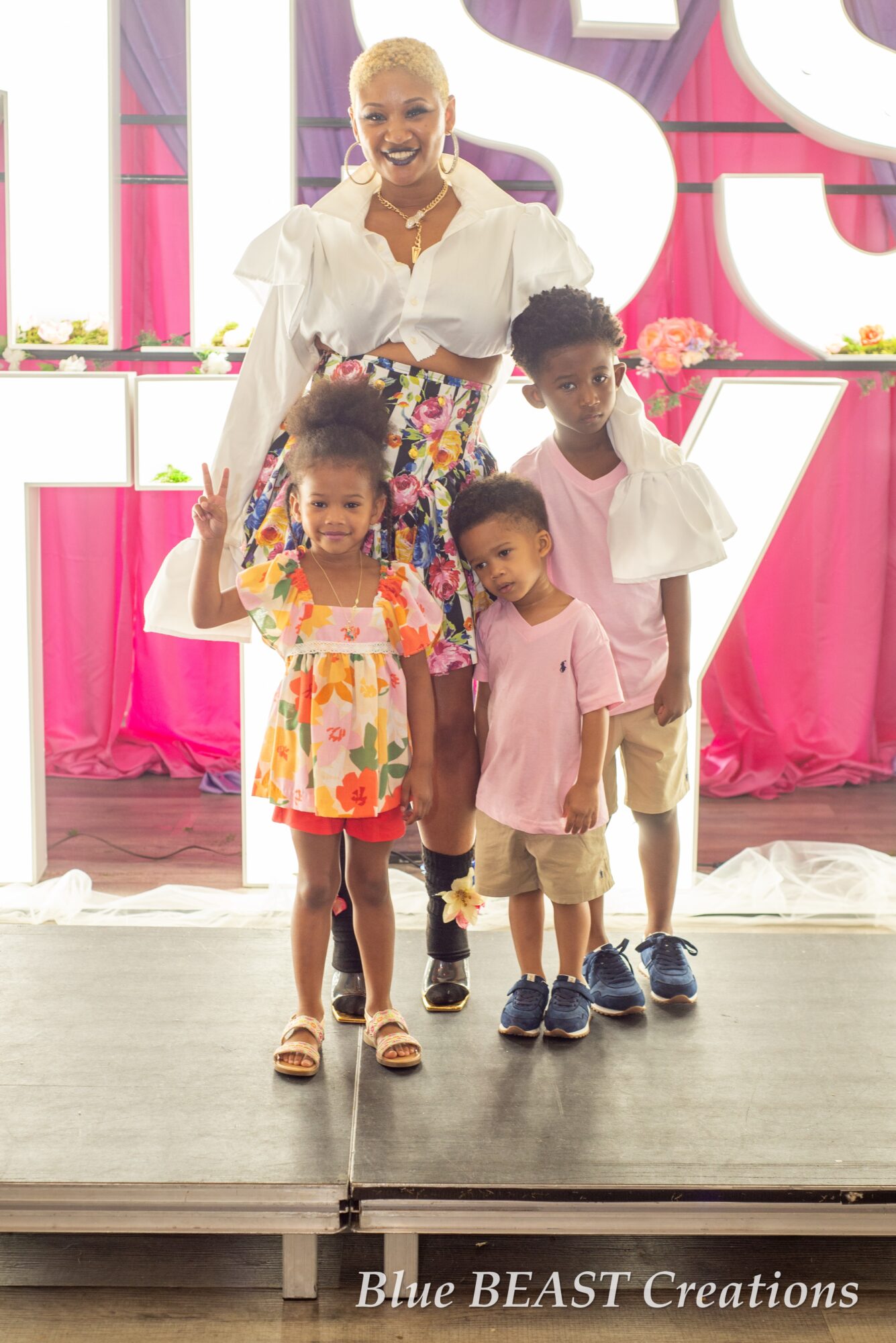 A woman with three children standing on a stage with pink and white decorations, smiling and posing for the photo.