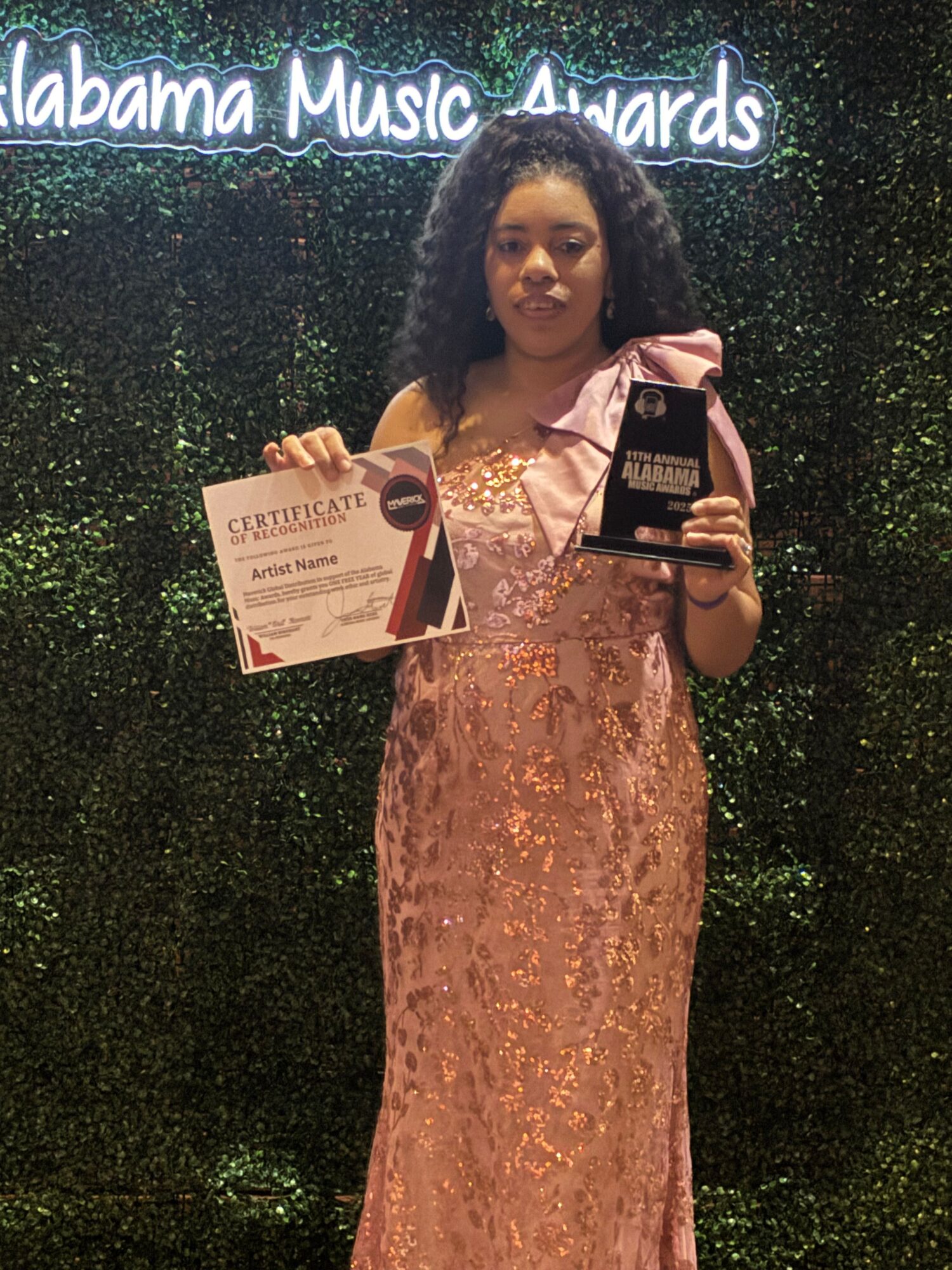 Woman in a pink dress holding a certificate and a phone, standing in front of a dark, glittery background.