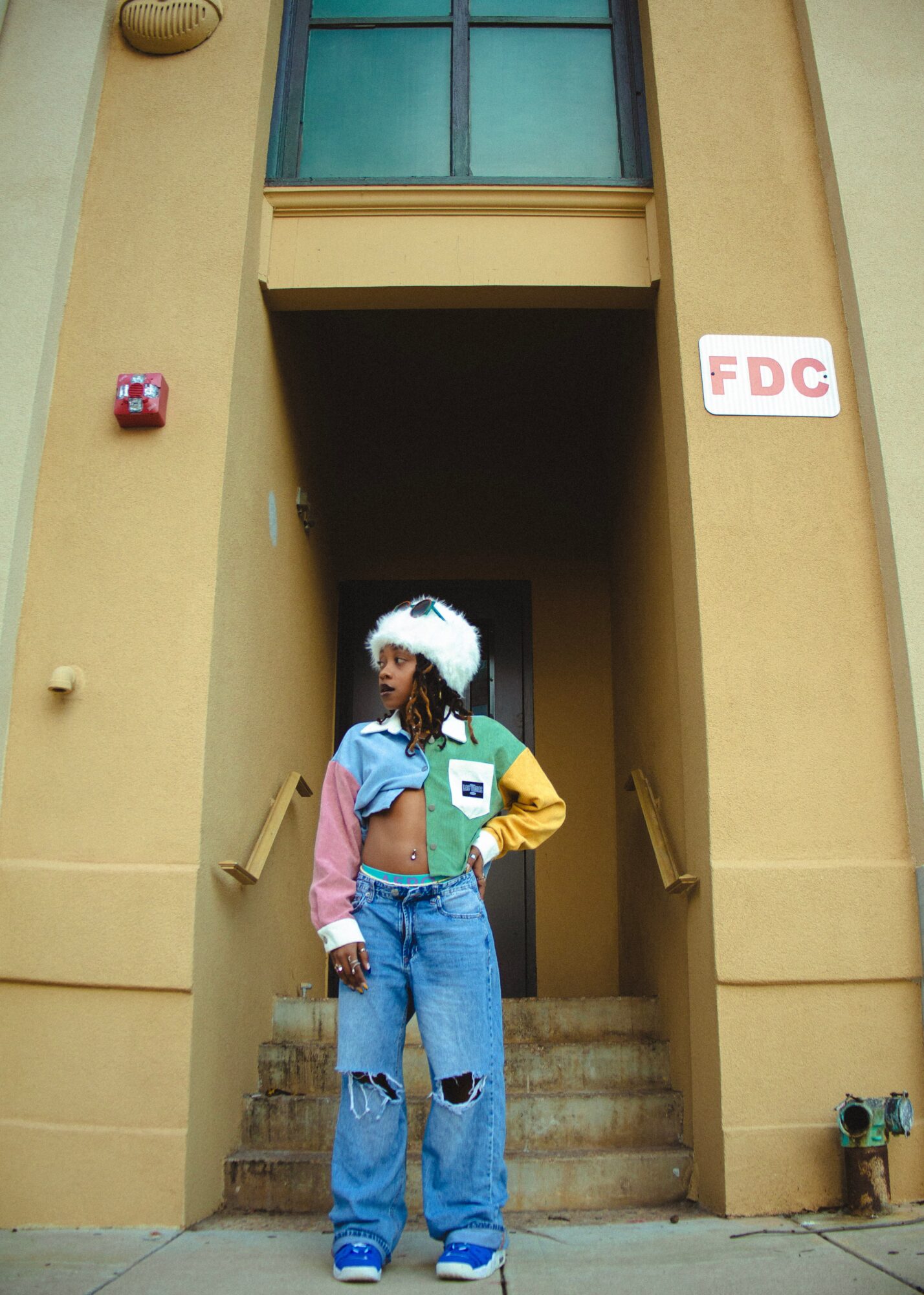 Person in colorful outfit standing on stairs in front of a building entrance with an FDC sign.