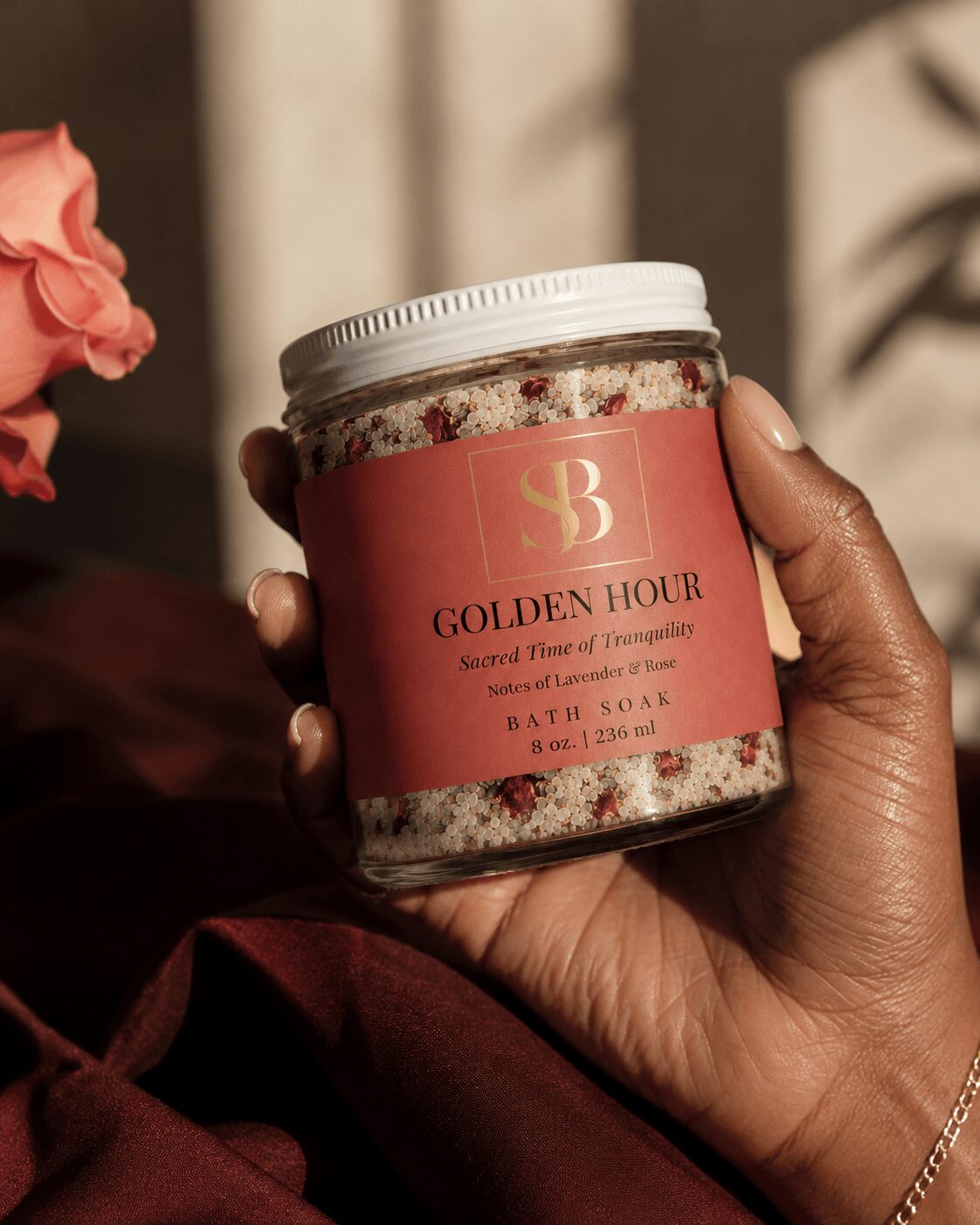Hand holding a jar labeled 'Golden Hour' with a pink label and white lid, background blurred.