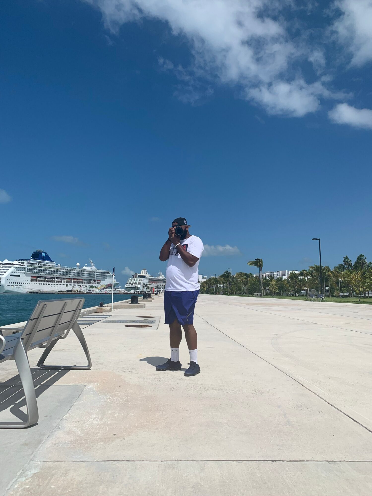 Person standing on a concrete surface holding a camera, with a boat and blue sky in the background.
