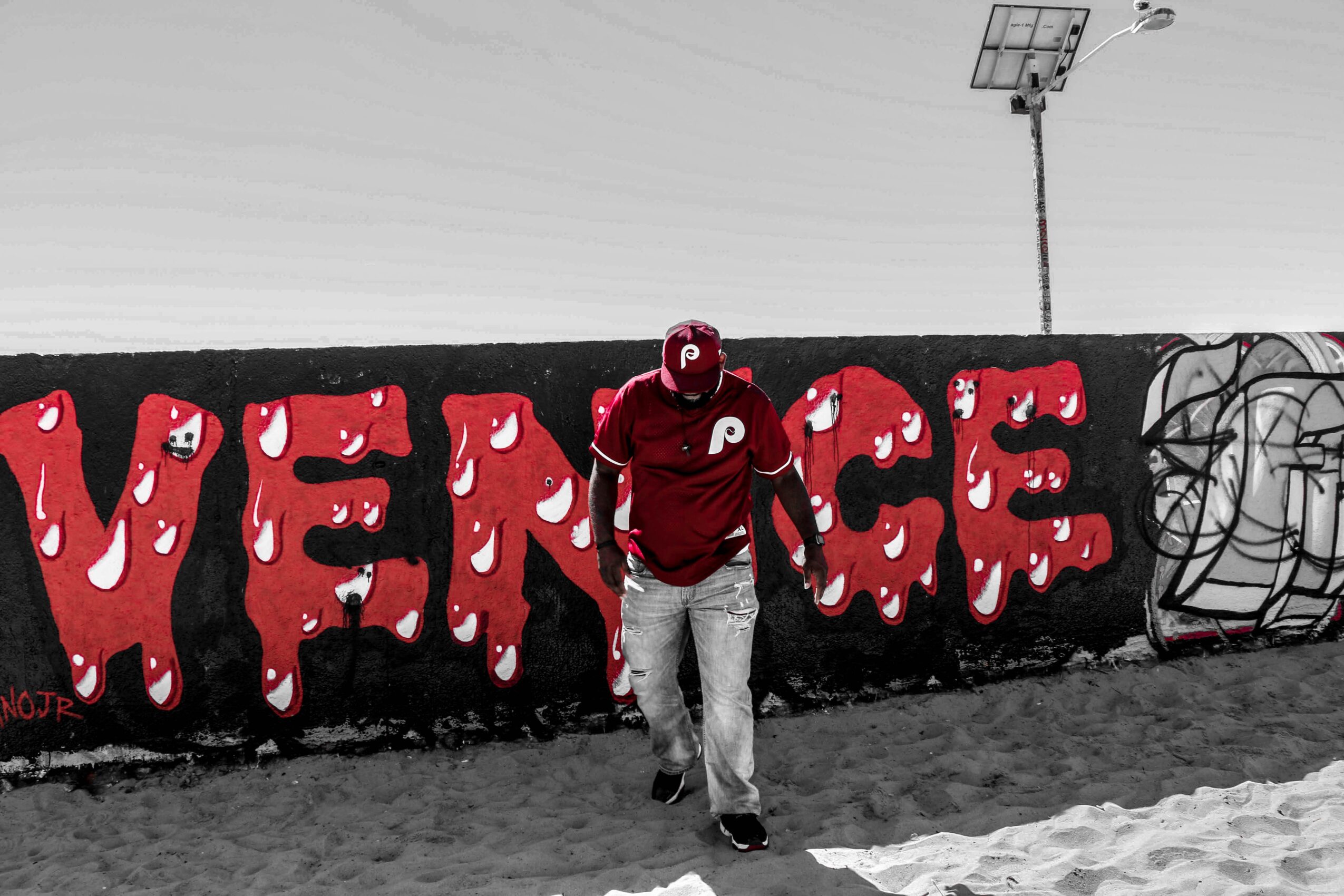 Person walking past a graffiti wall with large red letters spelling 'VENGE' on a black background.