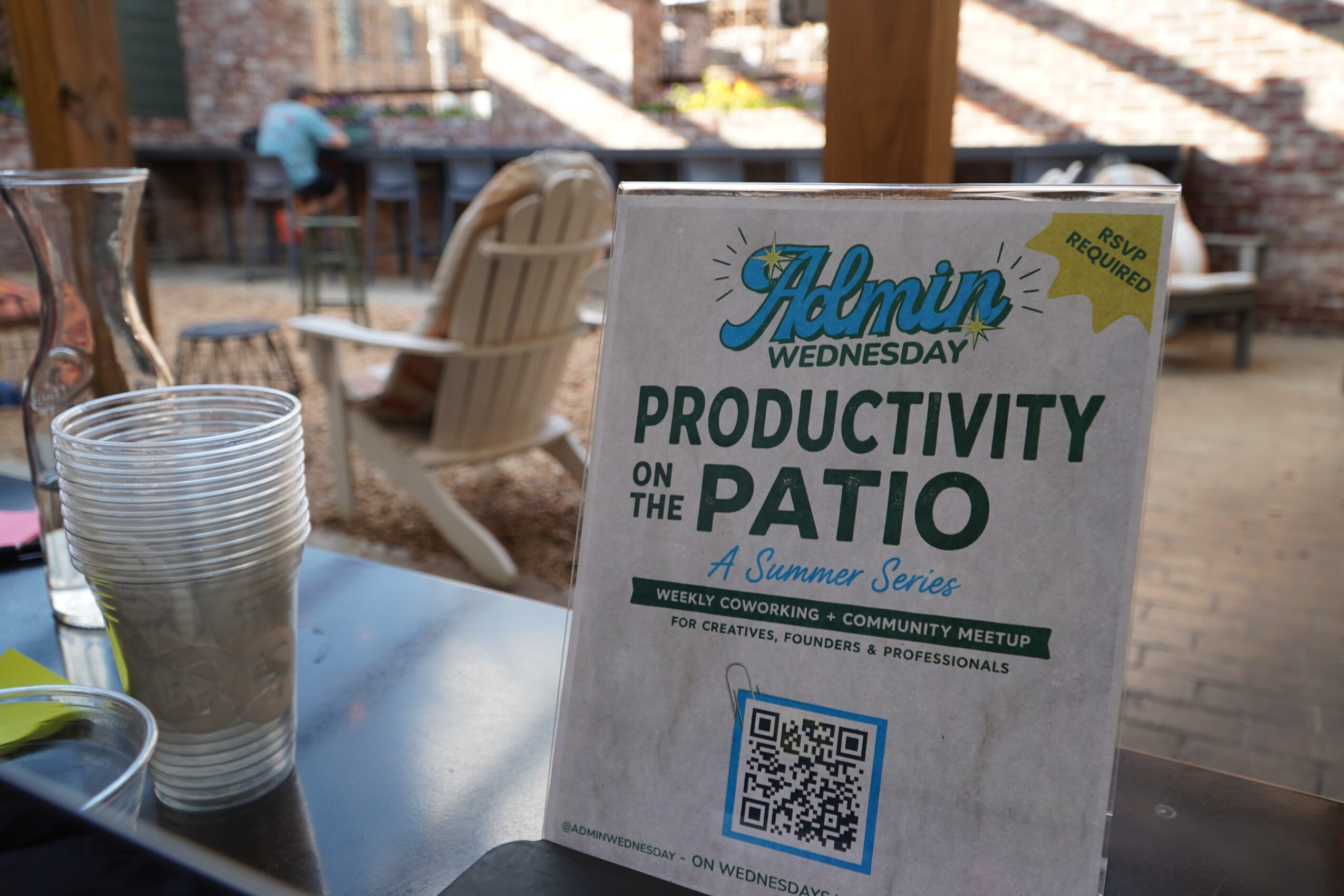 Sign on patio promoting productivity during summer series, with QR code, cups, and outdoor seating visible.