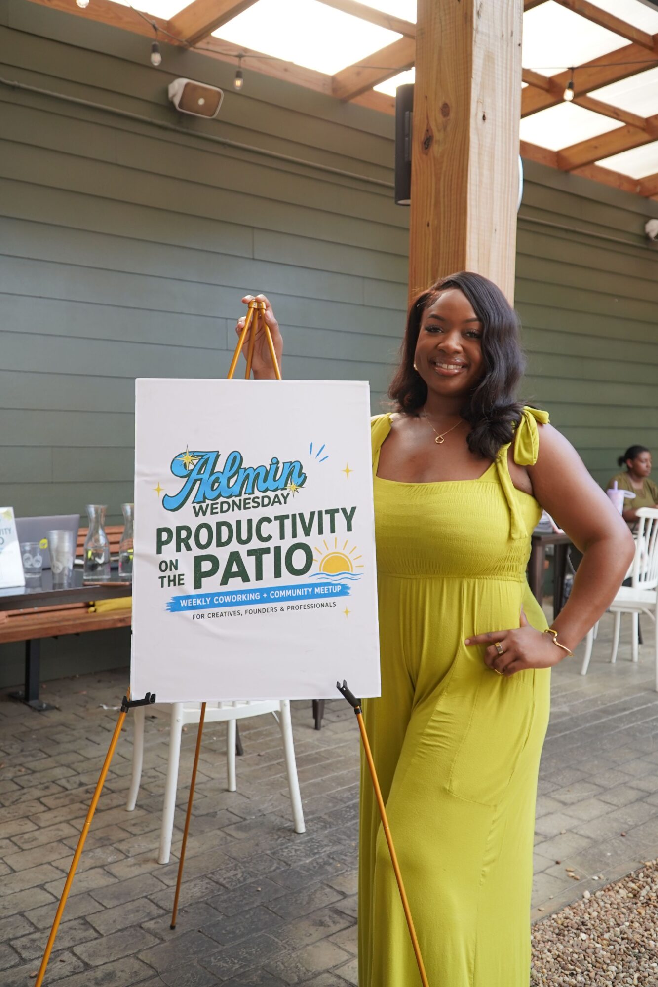 Woman in yellow dress standing next to a sign about community protection, indoors with wooden beams and green walls.