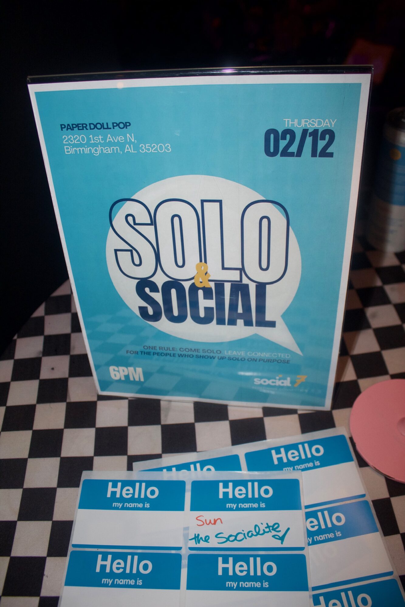 Event poster with blue and white design, displaying 'SOLO SOCIAL' and date '02/12', on a checkered surface.