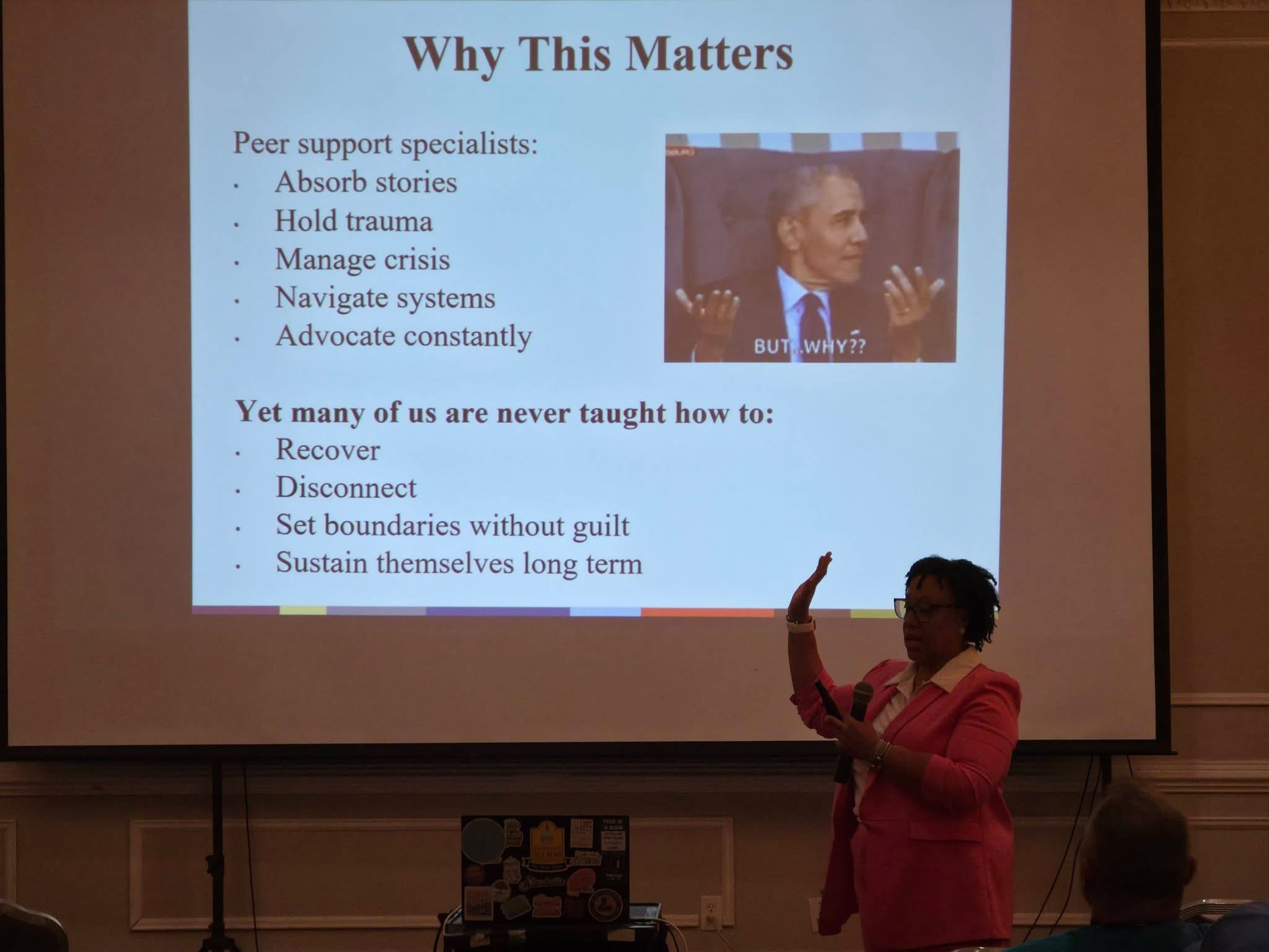 Person in pink blazer giving a presentation in front of a slide titled