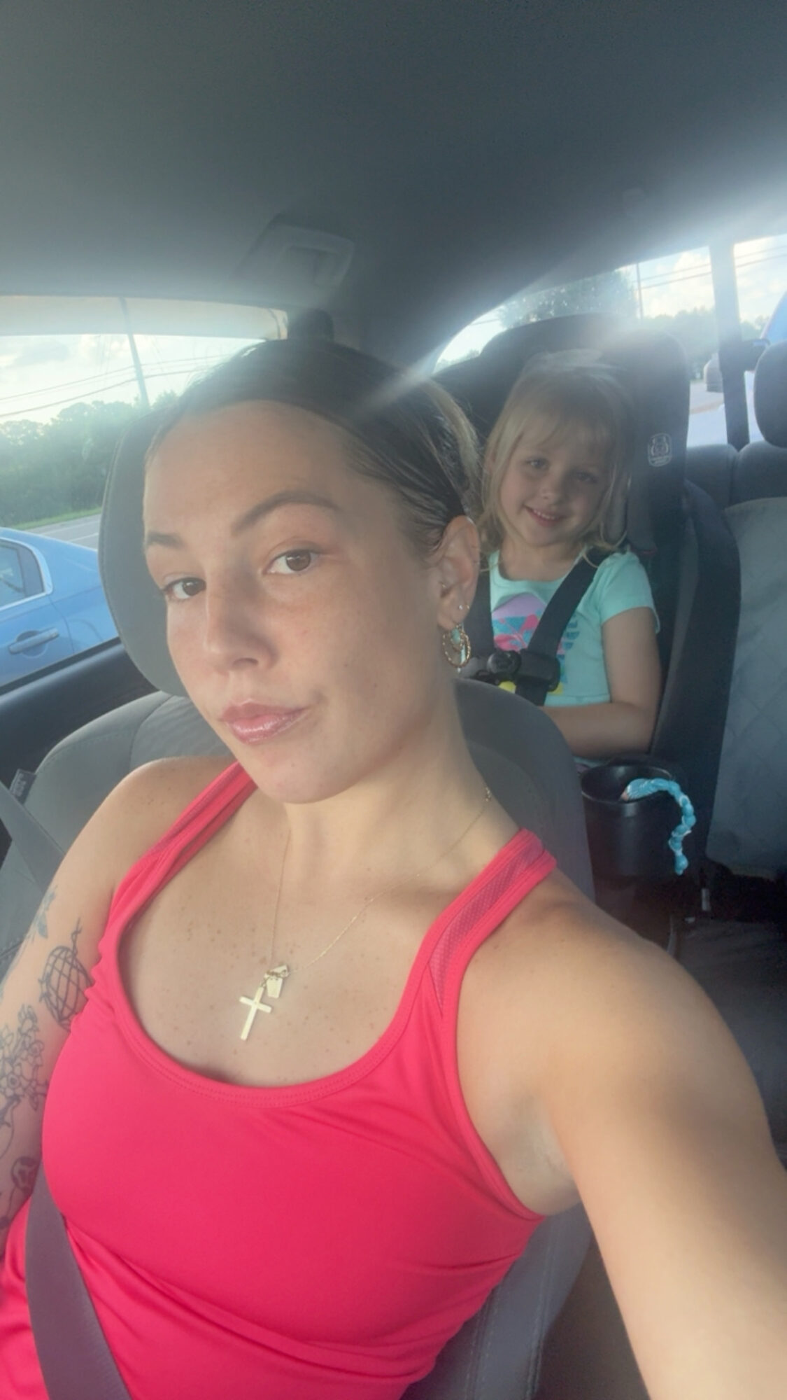 Woman taking selfie in car with a smiling girl in the back seat, both wearing casual clothes.