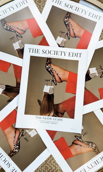 Magazine cover showing a woman's legs in leopard print high heels and an orange dress, with a white handbag, titled 'The Society Edit'.
