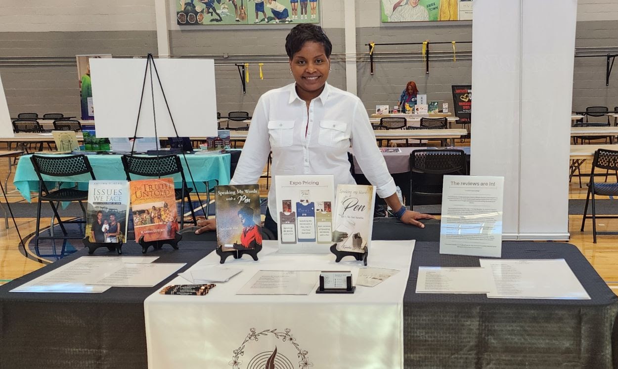 Person standing behind a table with promotional materials in a large indoor space.