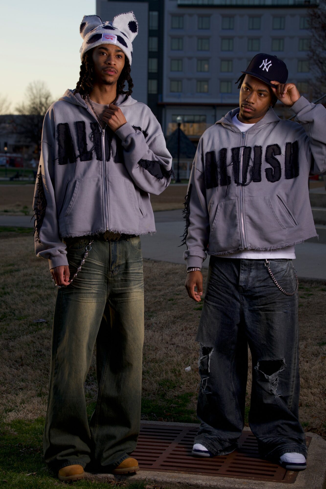 Two young people standing outdoors in casual clothing, one wearing a panda hat, in front of a building.