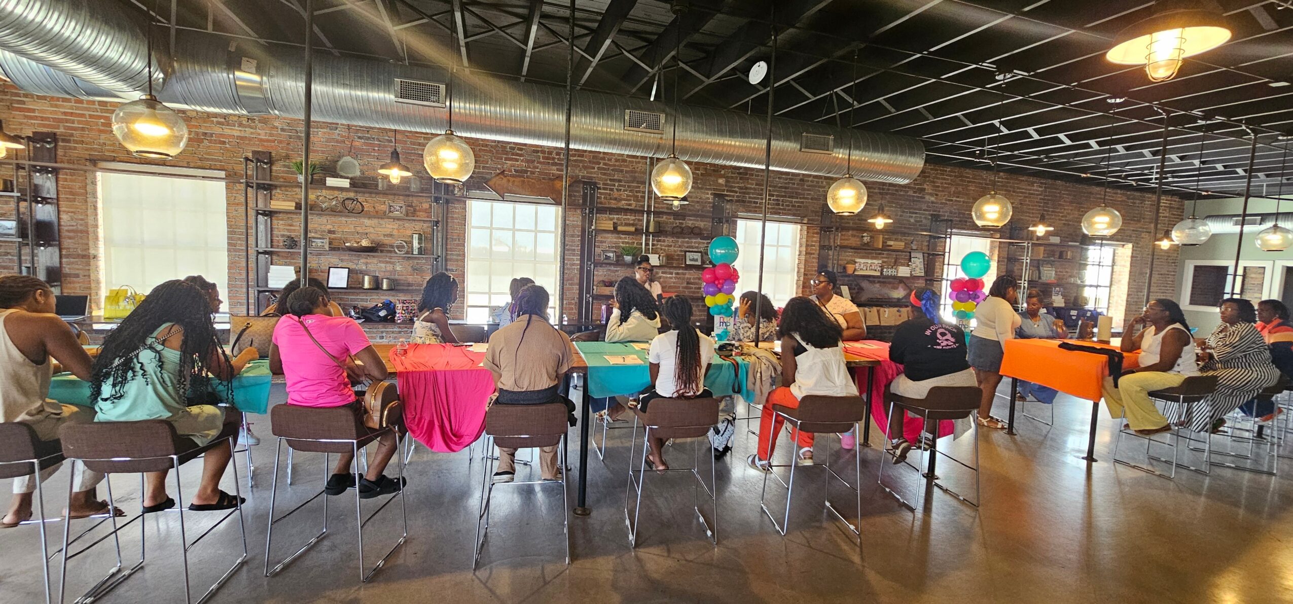 People seated at tables in a spacious, well-lit room with large windows and hanging lights.