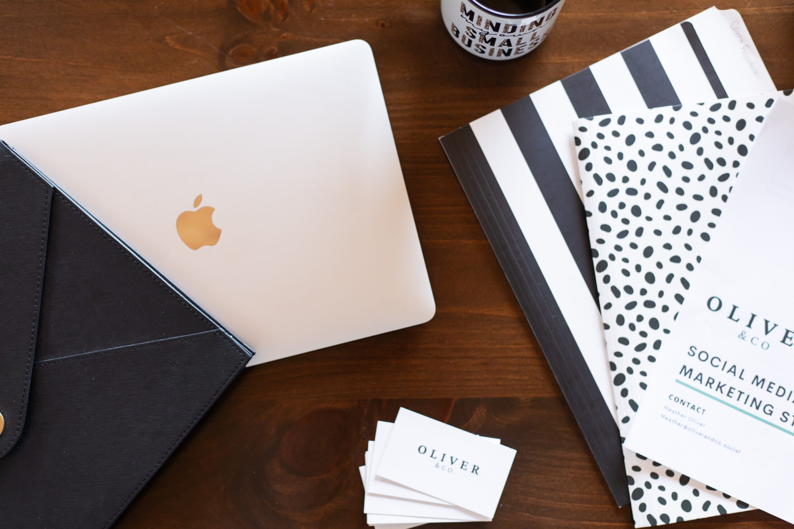 Laptop, notebooks, and a cup on a wooden table, with a black and white color scheme.