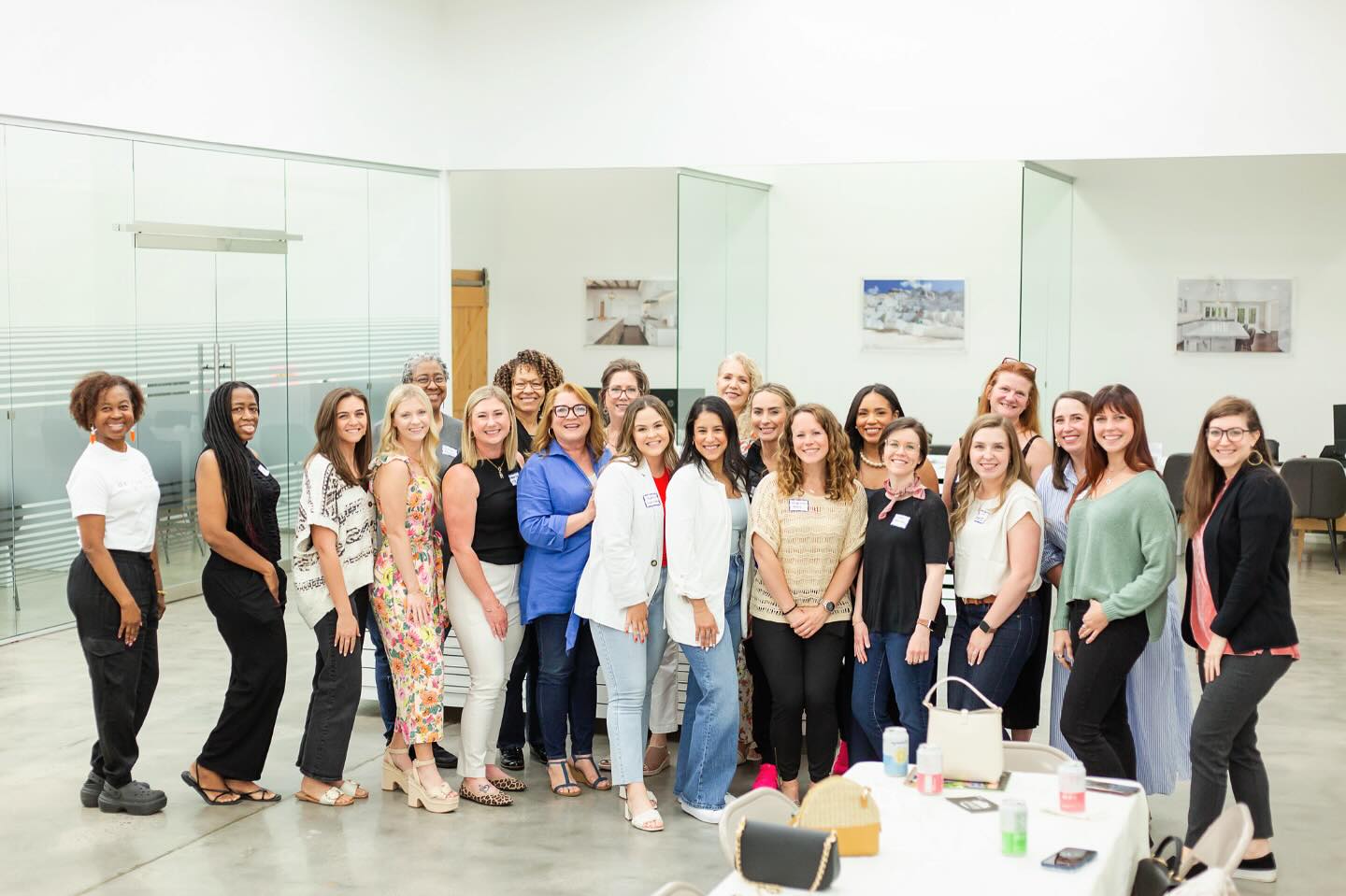 Group of women standing together in a gallery space, smiling, with artwork on the walls behind them.