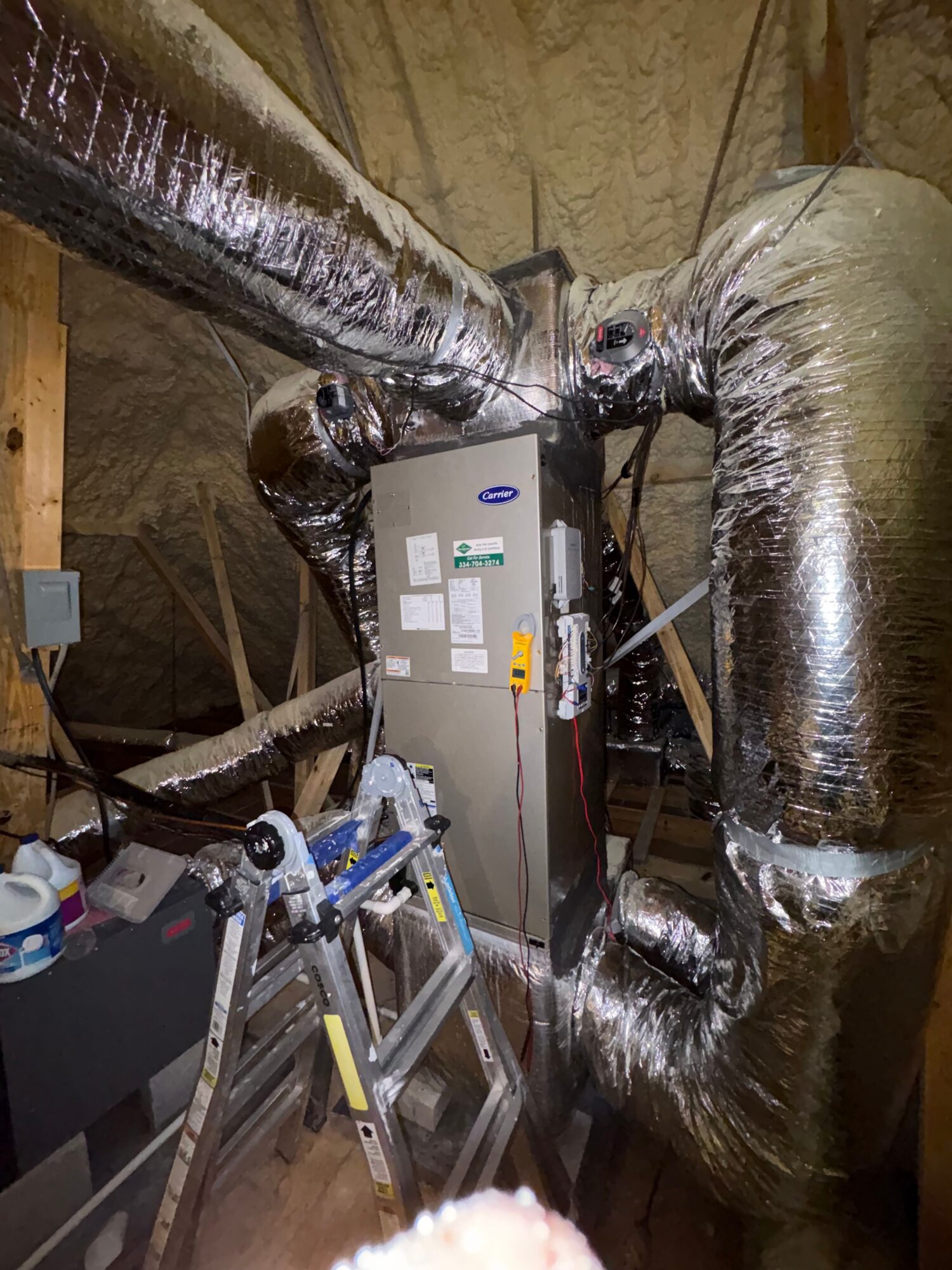 View of ductwork and HVAC equipment in an attic space, with insulation and tools visible.