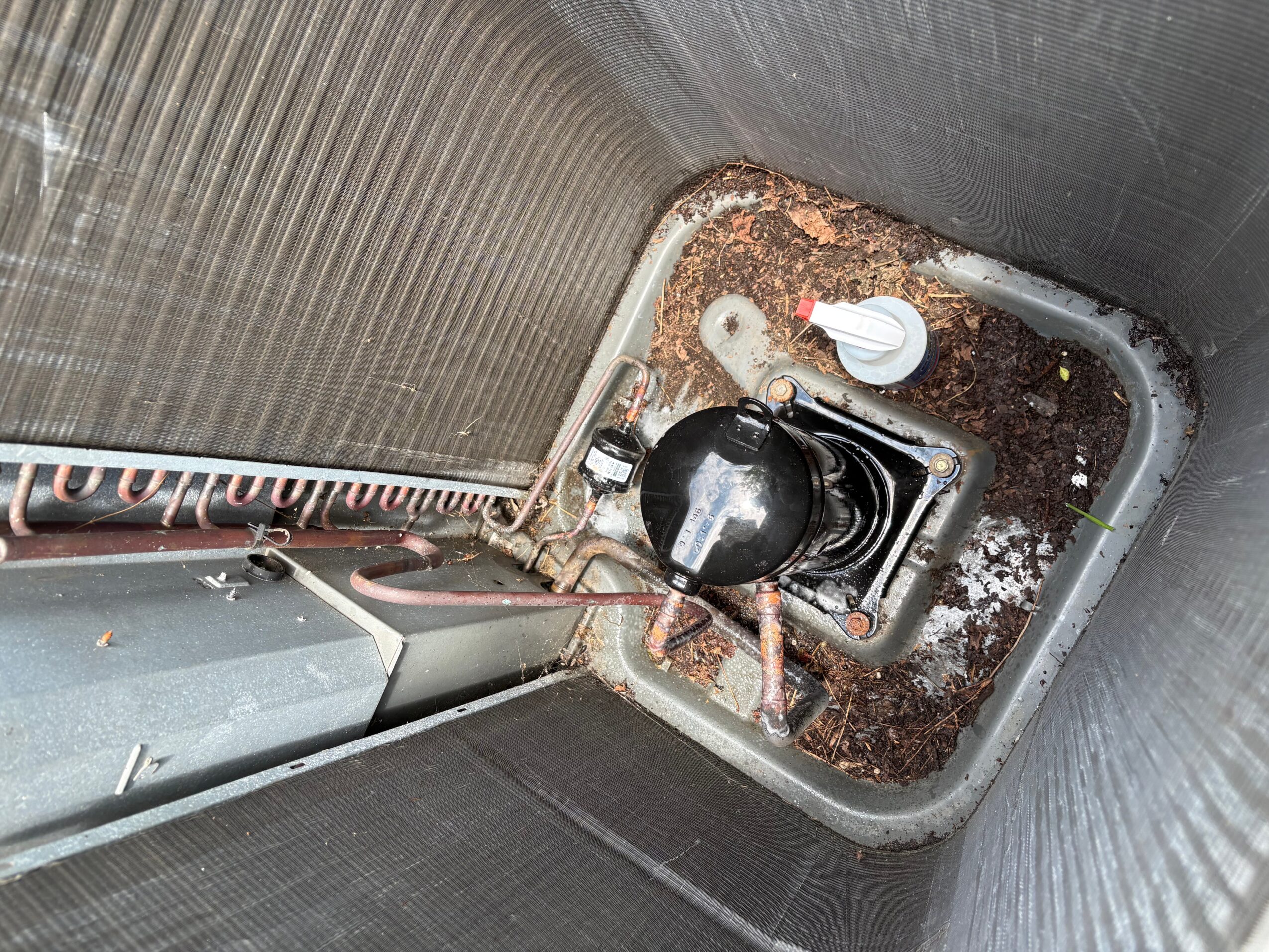 View of a cooling tower's interior base with a black pipe, white valve, and surrounding soil or debris.