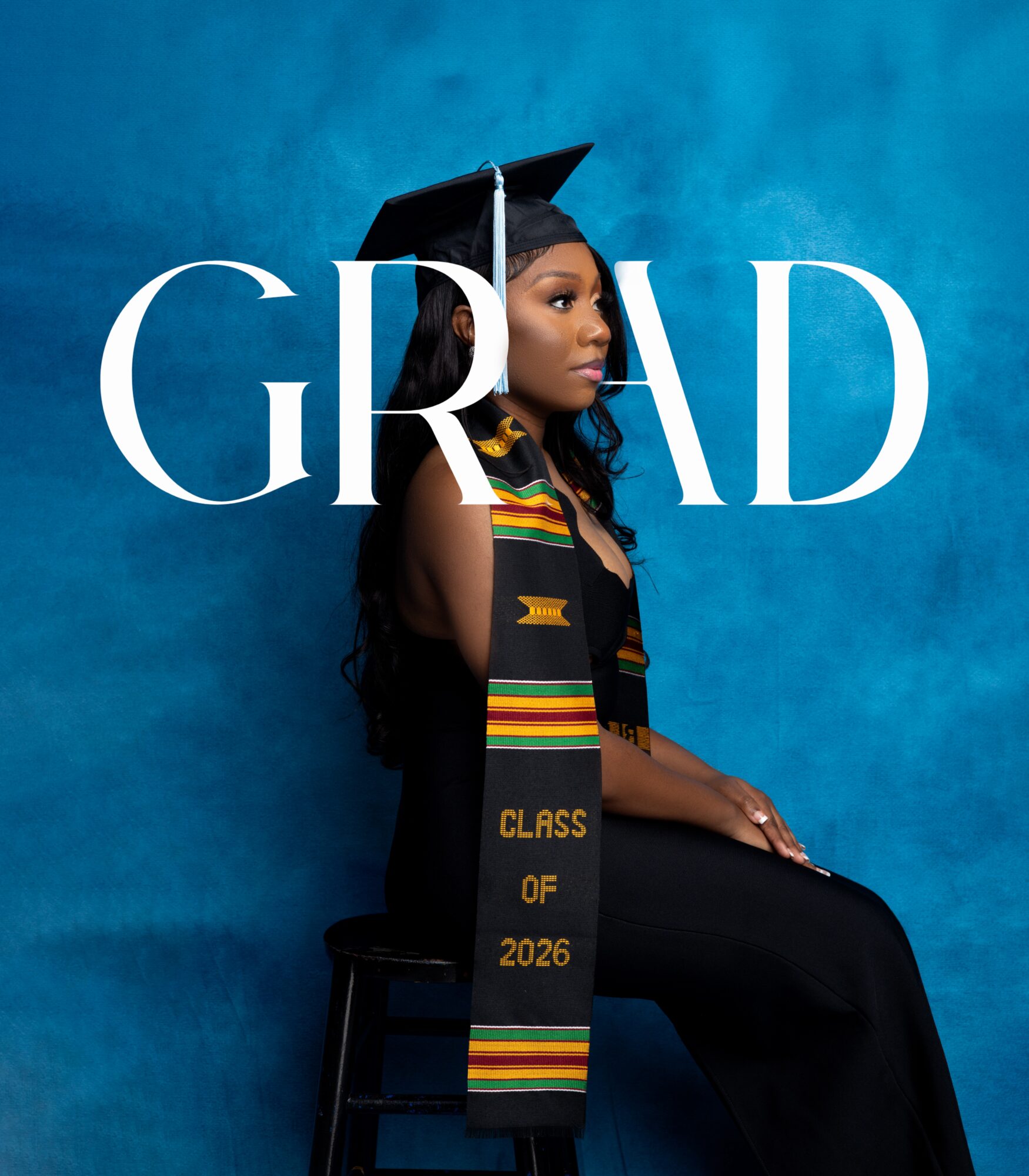 Young woman in graduation cap and gown, sitting against blue background, with large white 'GRAD' text overlay.
