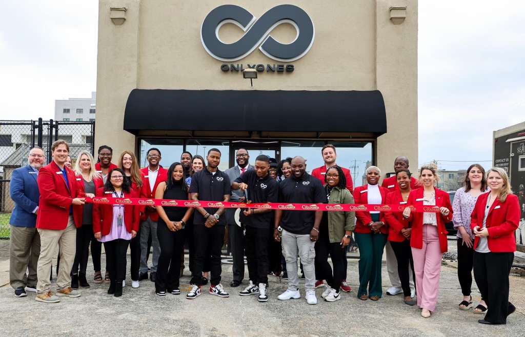 Group of people in red and black clothing standing outside a building with a large infinity symbol sign, holding a red ribbon.