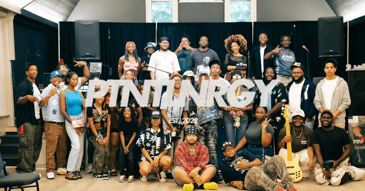 Group of people holding a large sign that reads 'PRINTING' in a room with black curtains and speakers.