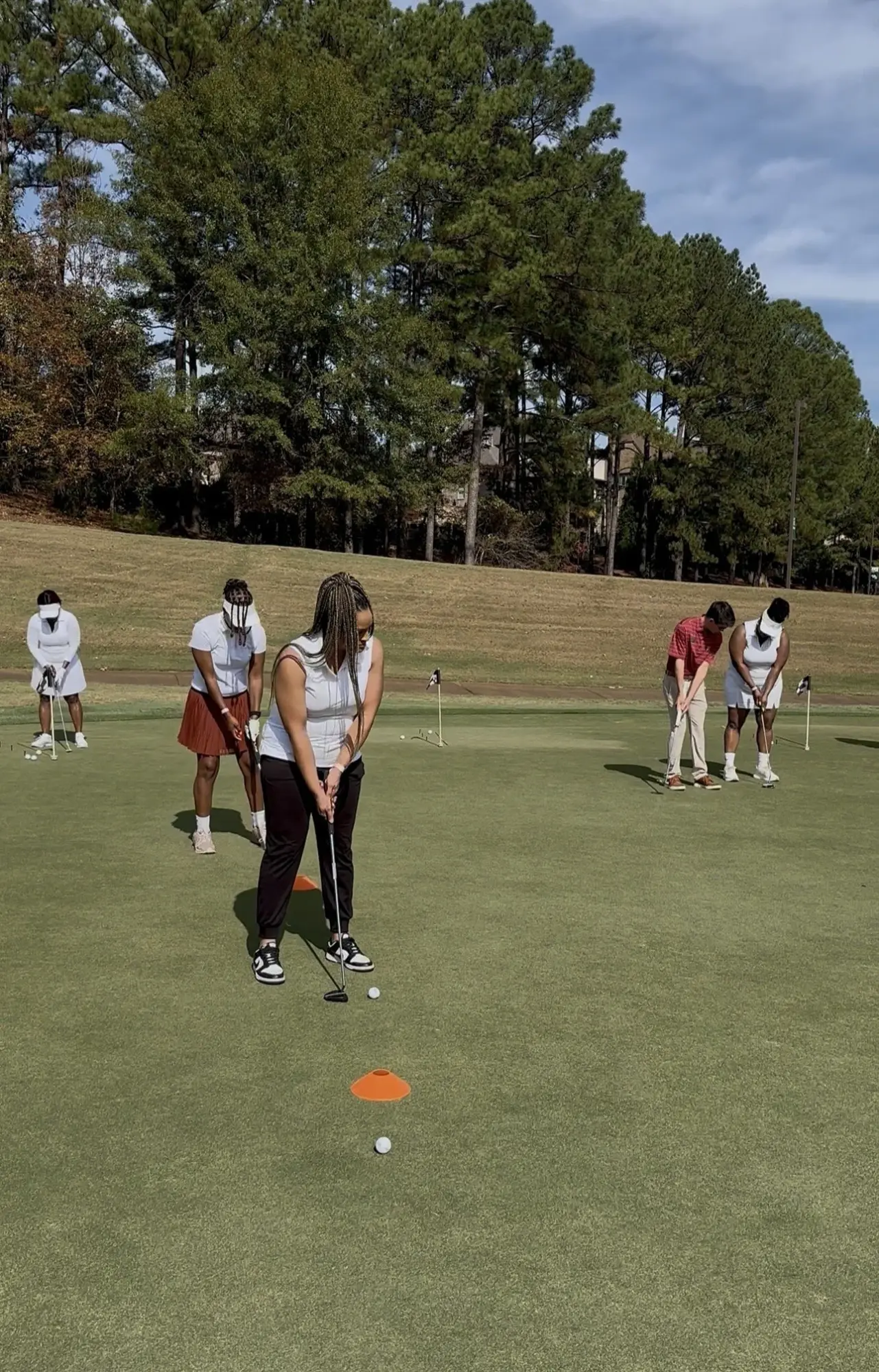 Group of children playing mini-golf on a green field with trees in the background.