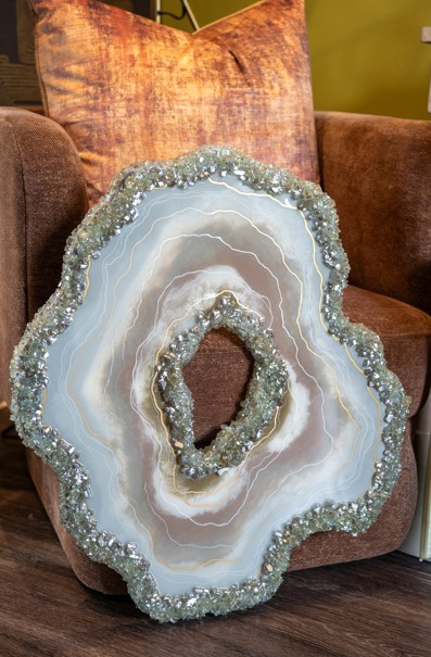 Decorative agate slice with crystal embellishments leaning against a brown armchair, with a green wall in the background.