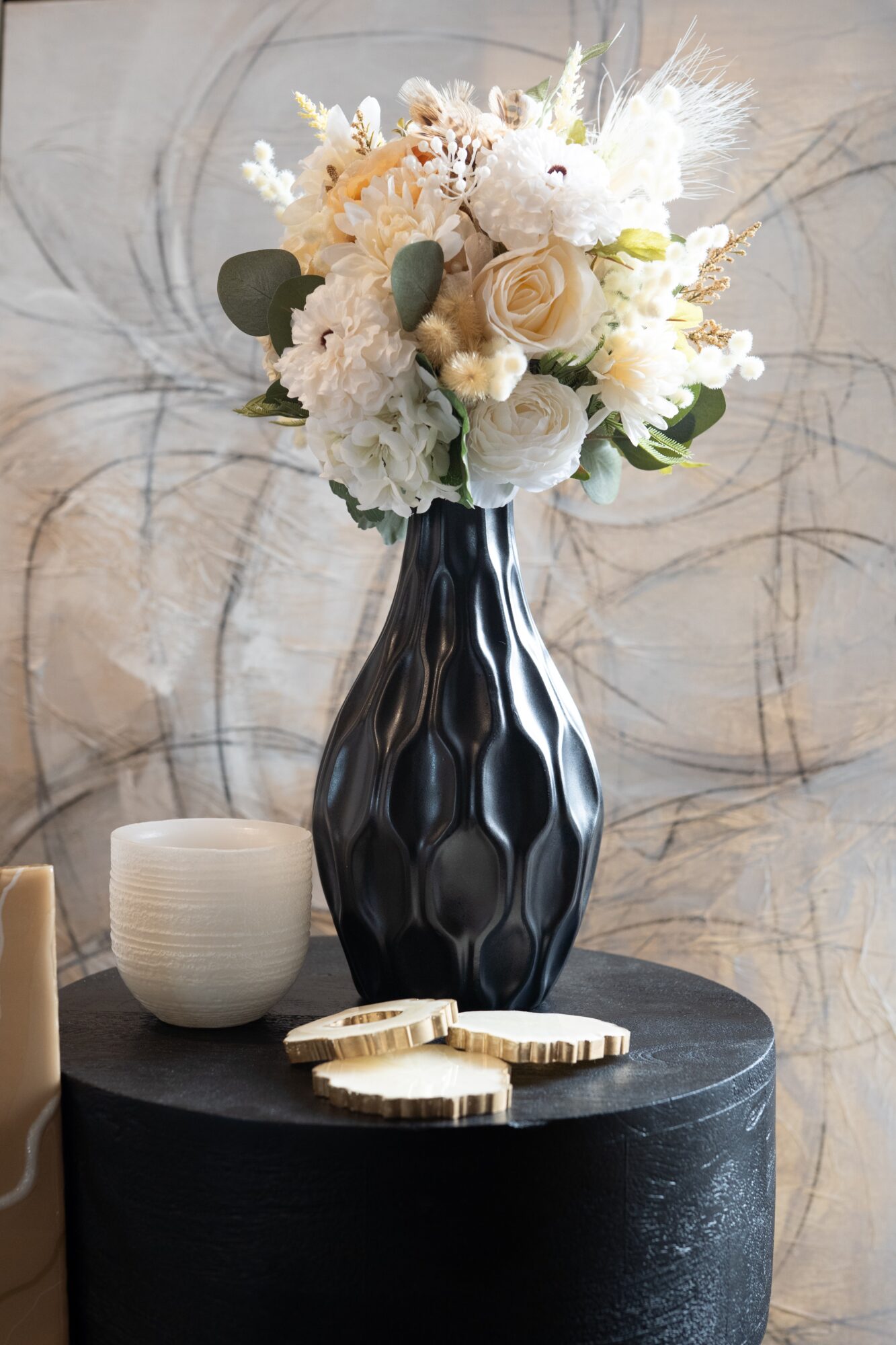 Vase with white flowers on a black table, with a small white bowl and wooden decorative objects nearby.