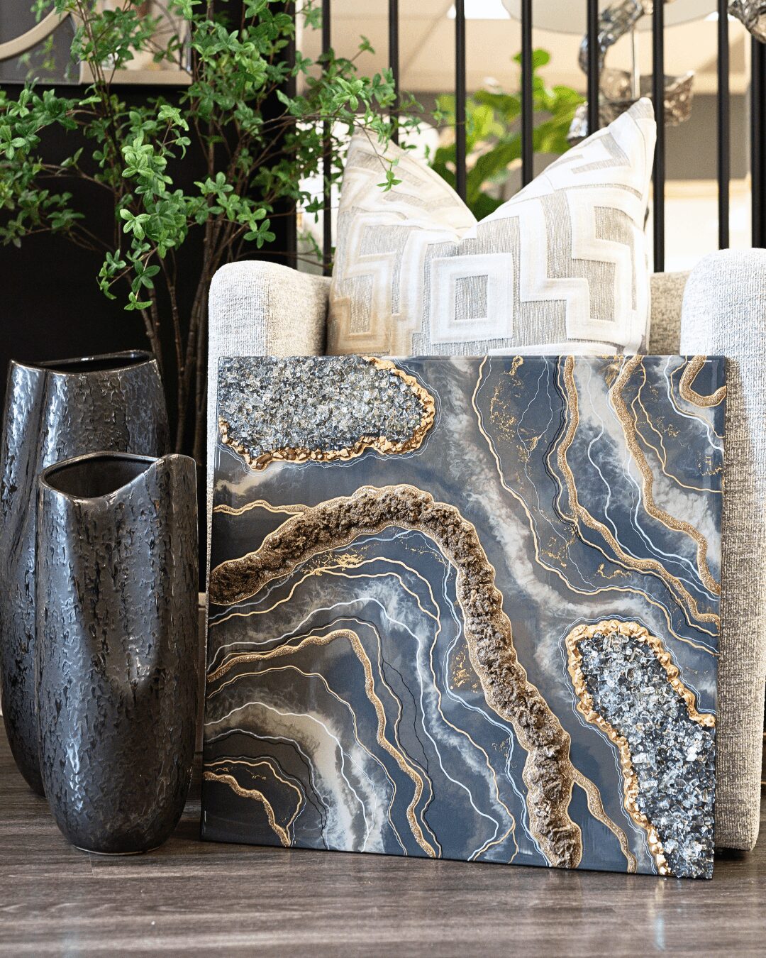 Decorative marble slab with blue, gold, and brown patterns leaning against a sofa with pillows, outdoors with plants and a fence.