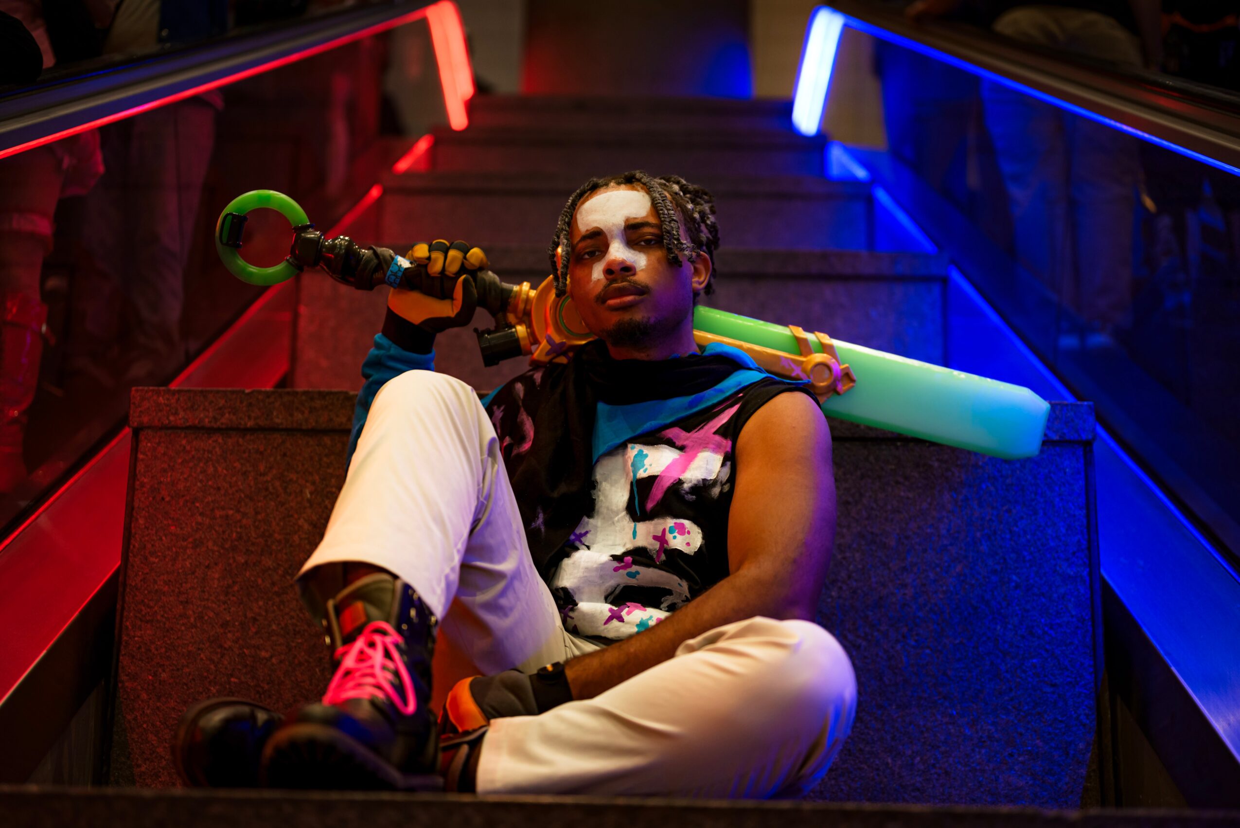 Person sitting on stairs holding a toy gun, with colorful lighting and a neon glow, wearing casual clothing and sneakers.