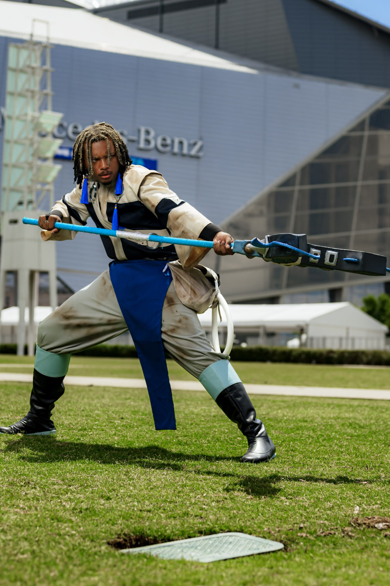 Person in costume holding a staff, standing on grass in front of a modern building with Mercedes-Benz logo.