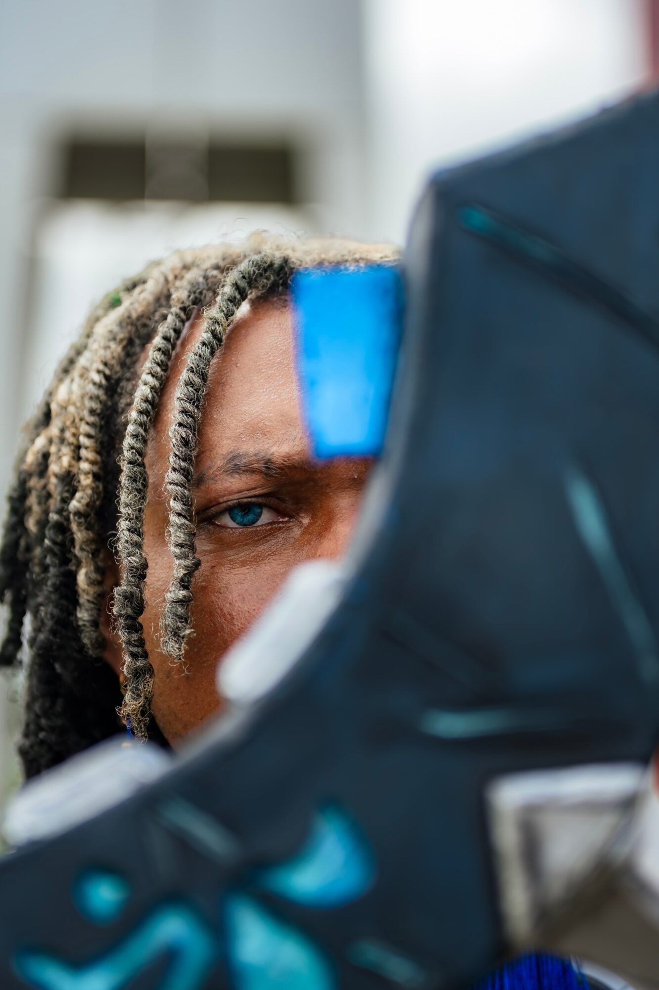 Person with dreadlocks looking through a medical eye examination device, with a blue sticker on their forehead.