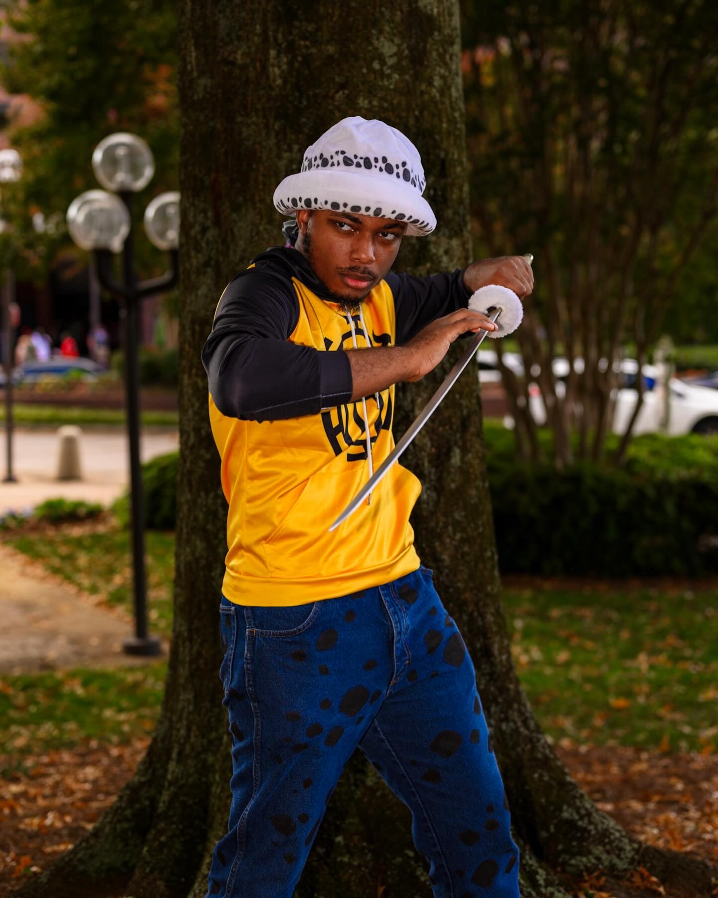 Child wearing a white hat and yellow jacket, holding a white object, standing outdoors near a tree.