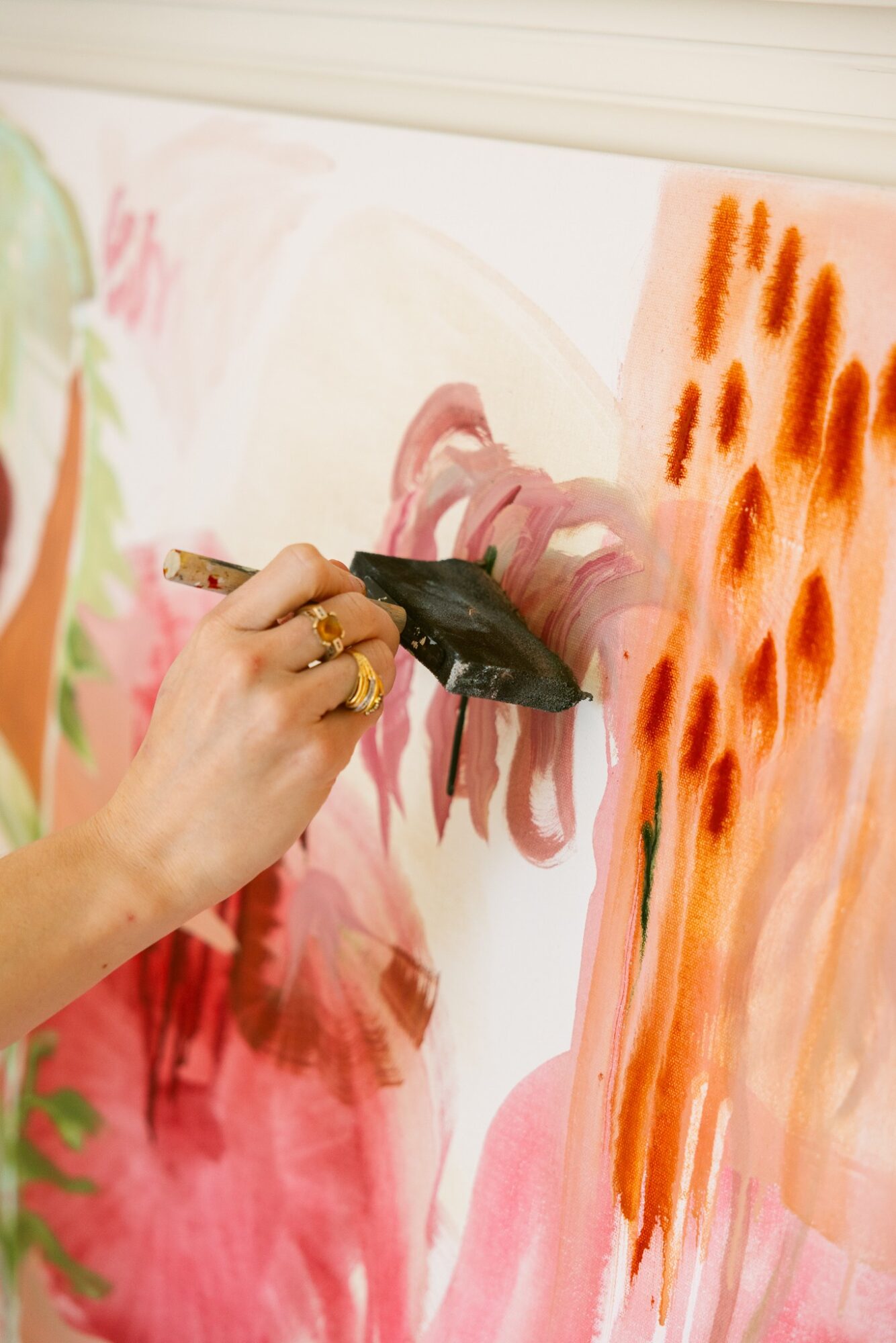 Person painting on a canvas with pink, orange, and green colors, holding a brush and applying paint.