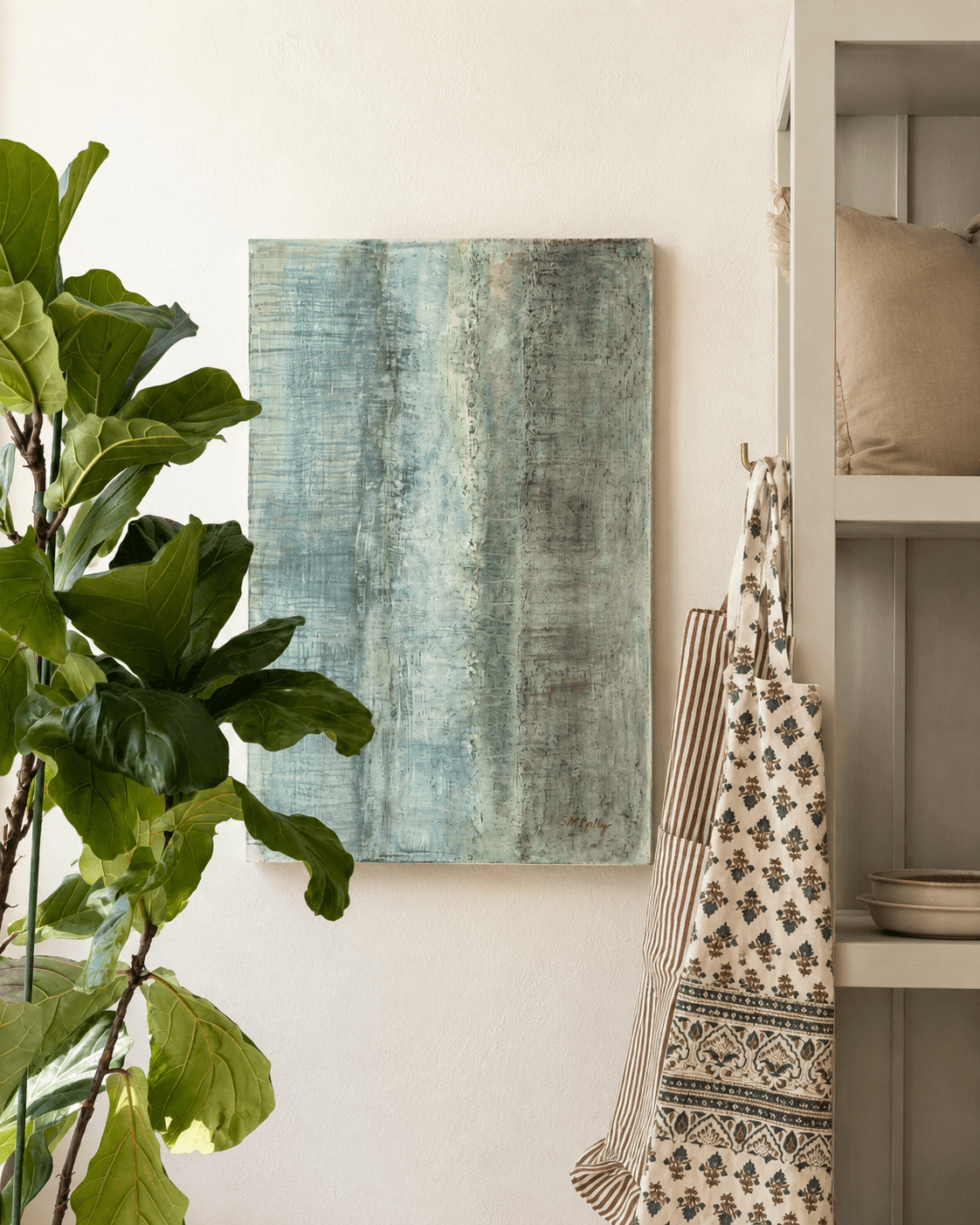 Wall with abstract blue and green painting, large green plant, and shelves with pillows and dishes, in a cozy room.